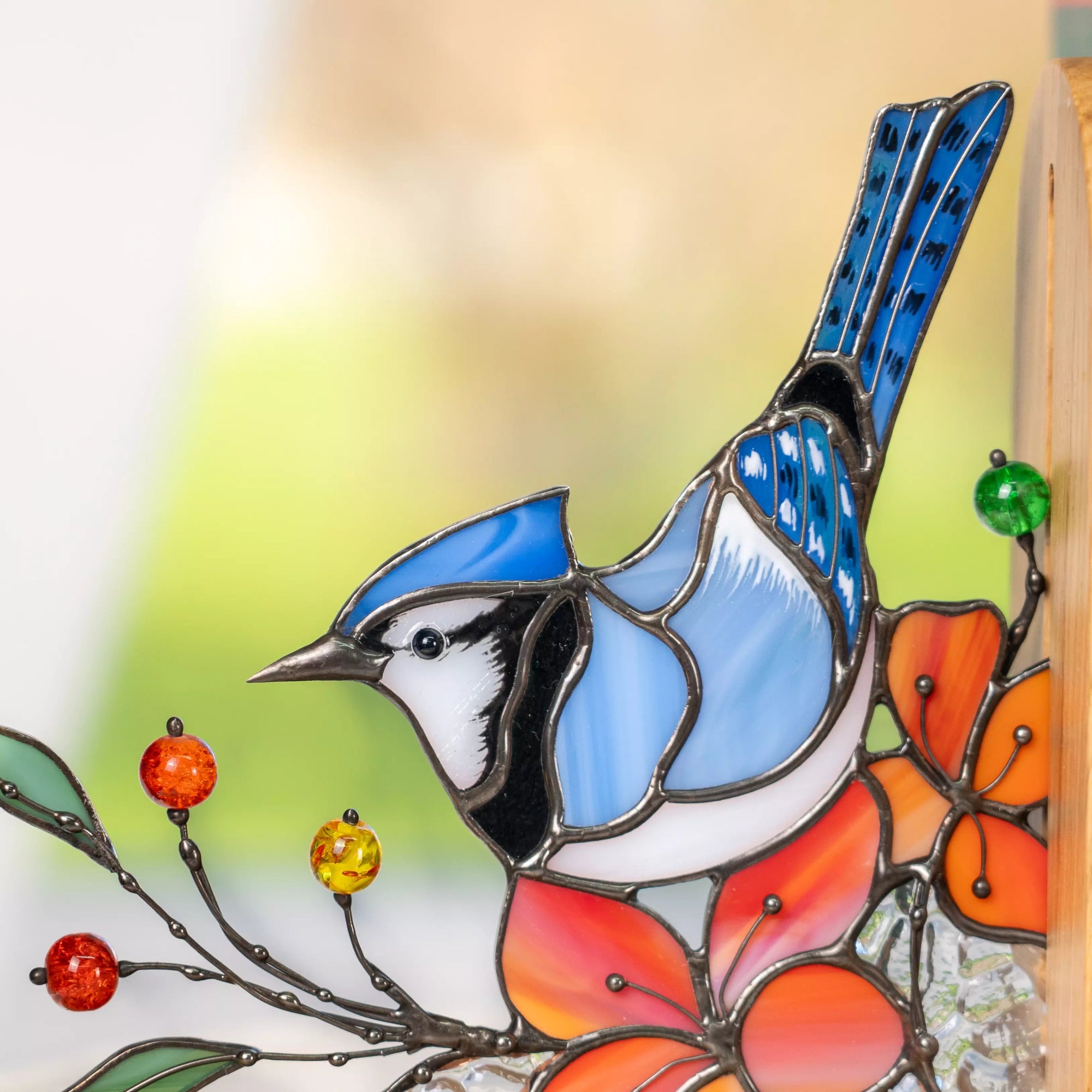 Close-up of a blue jay stained glass bird with glass beads accents on thin metal branches.