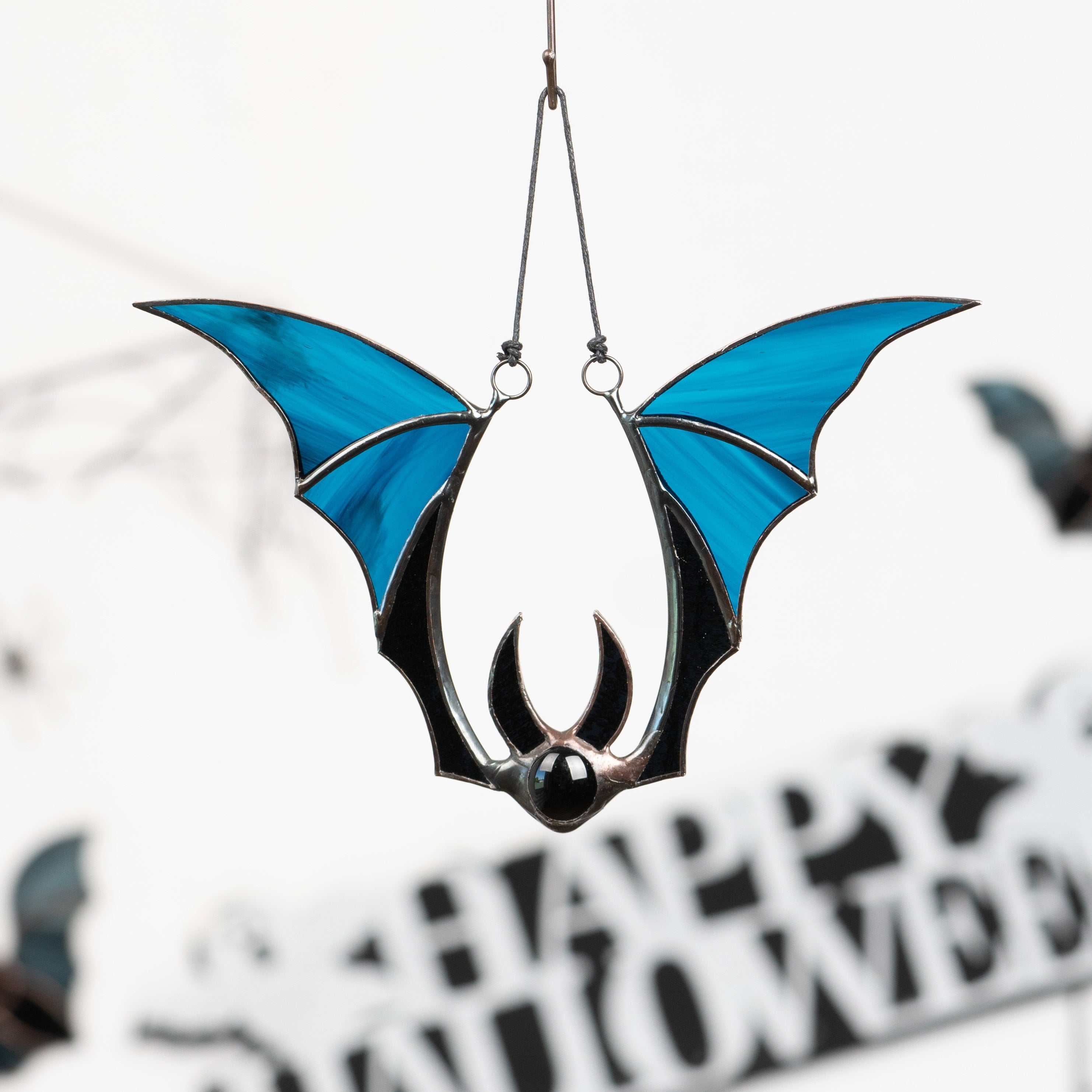 Blue-winged stained glass bat hanging in front of “Happy Halloween” decor with other bats in the background