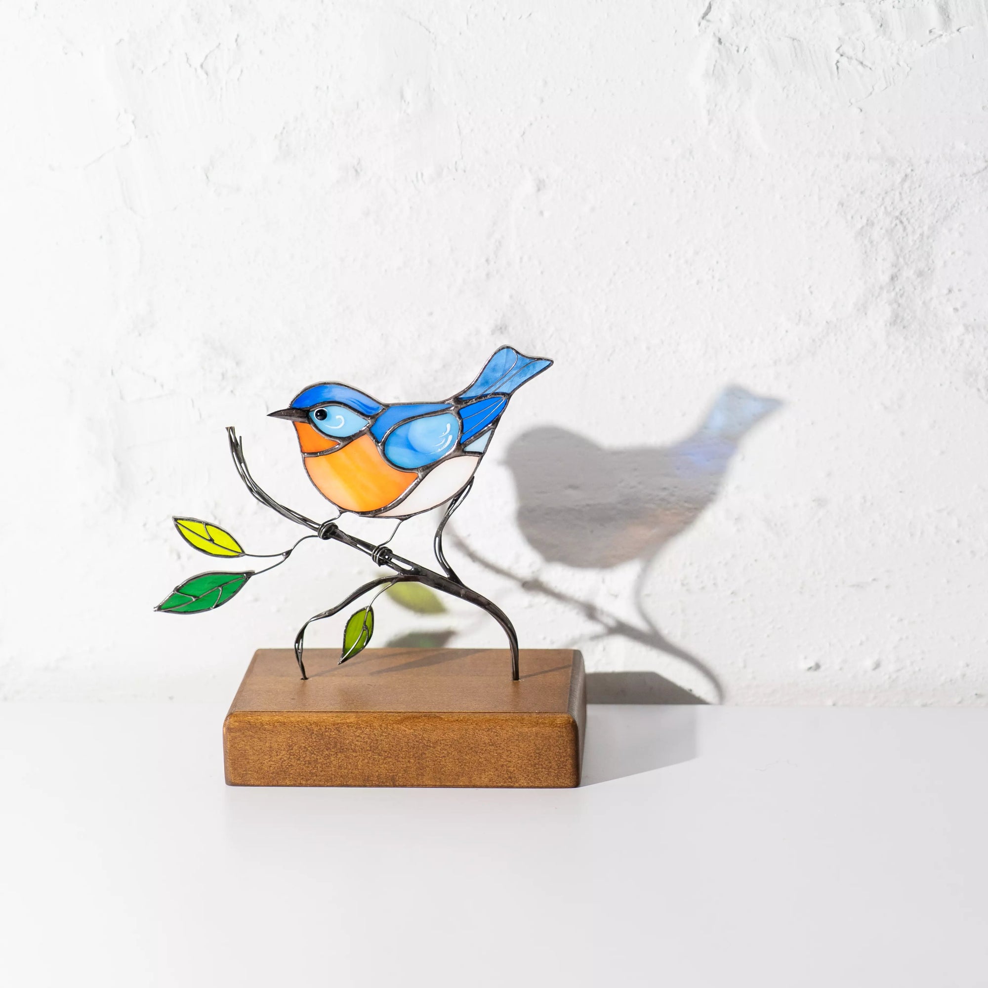 Artistic bluebird figure in stained glass with wirework and green glass leaves on wood block