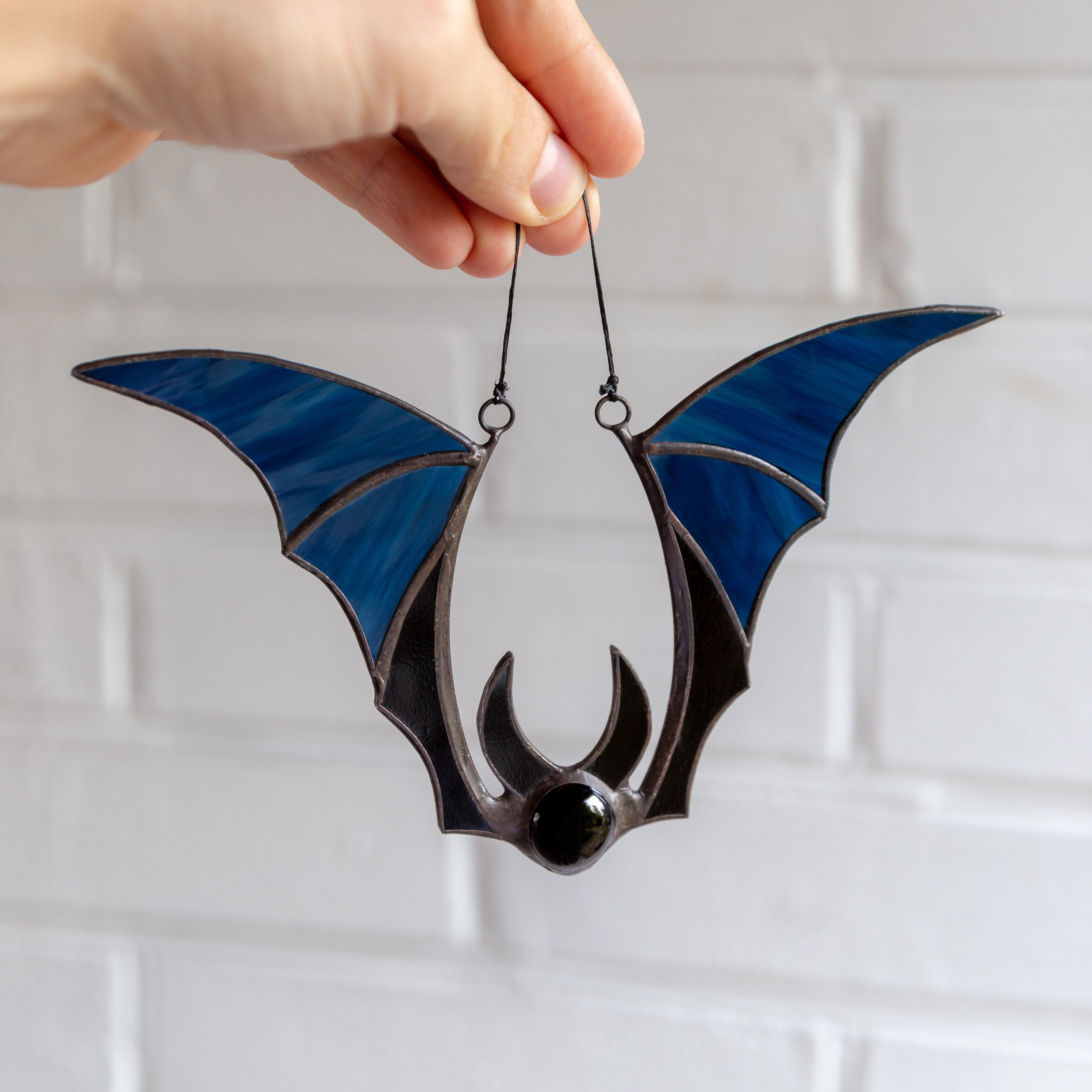 Blue and black stained glass bat held by hand against white brick wall background