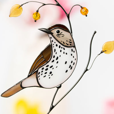 Close-up of handcrafted stained glass wood thrush with golden glass leaf and bead details