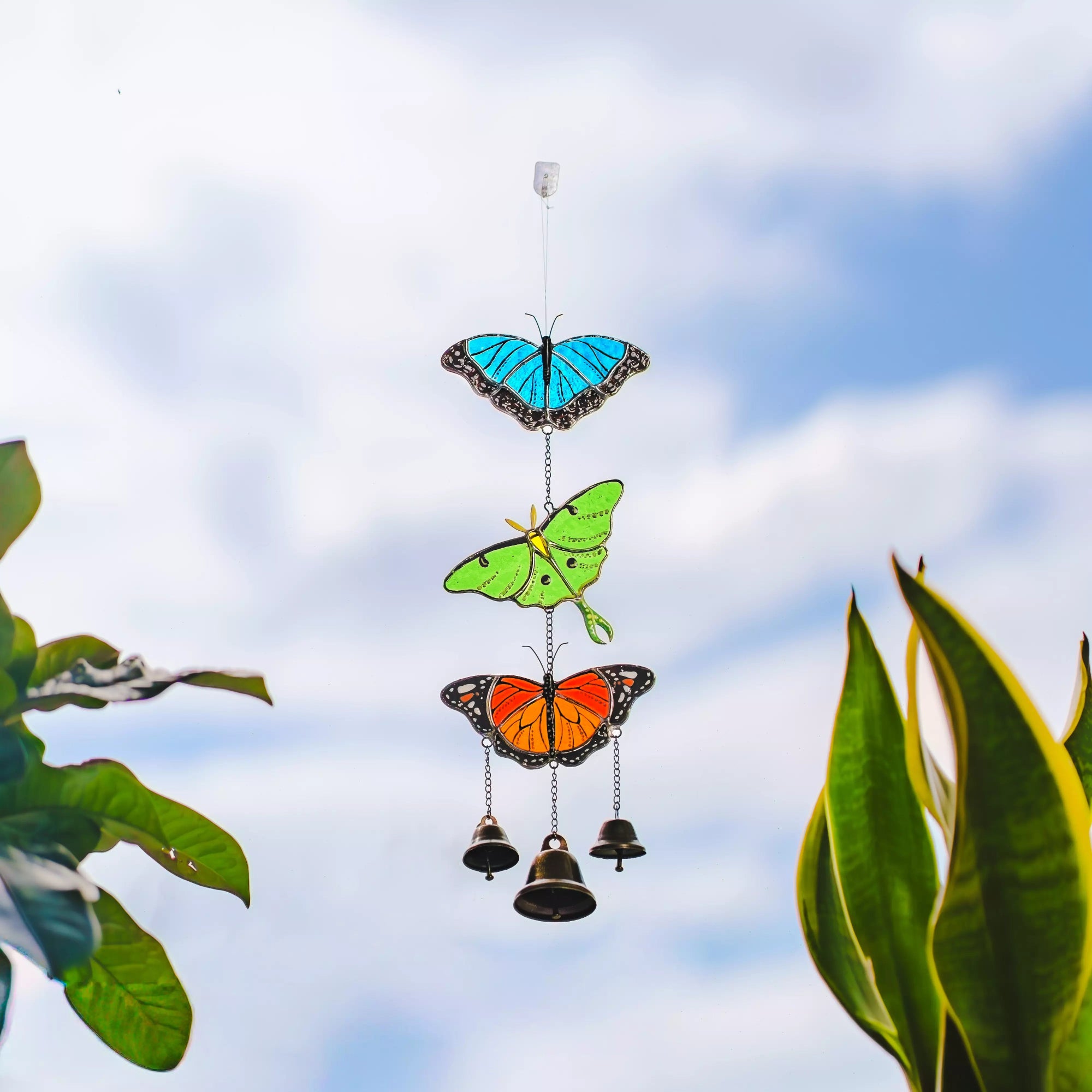 Butterfly-shaped stained glass wind chime with bells against a blue sky background