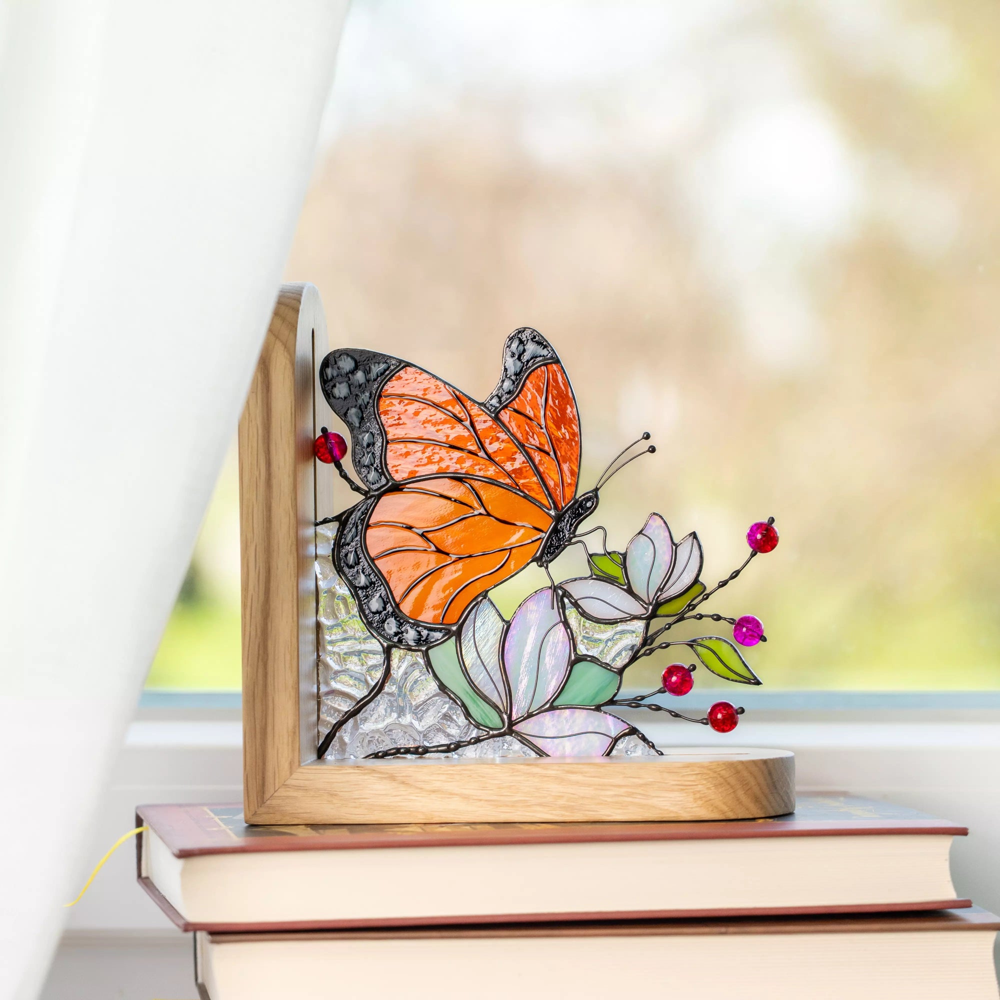 Butterfly stained glass bookend standing on stacked books near a window with soft natural light.