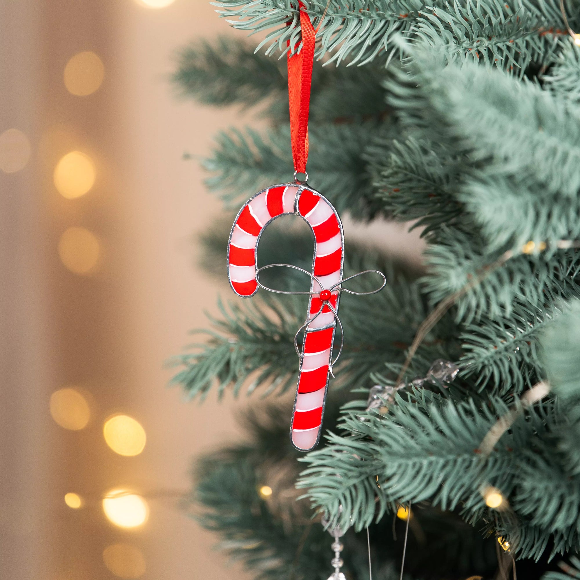 Candy cane stained glass suncatcher hanging on a Christmas tree with blurred lights in the background