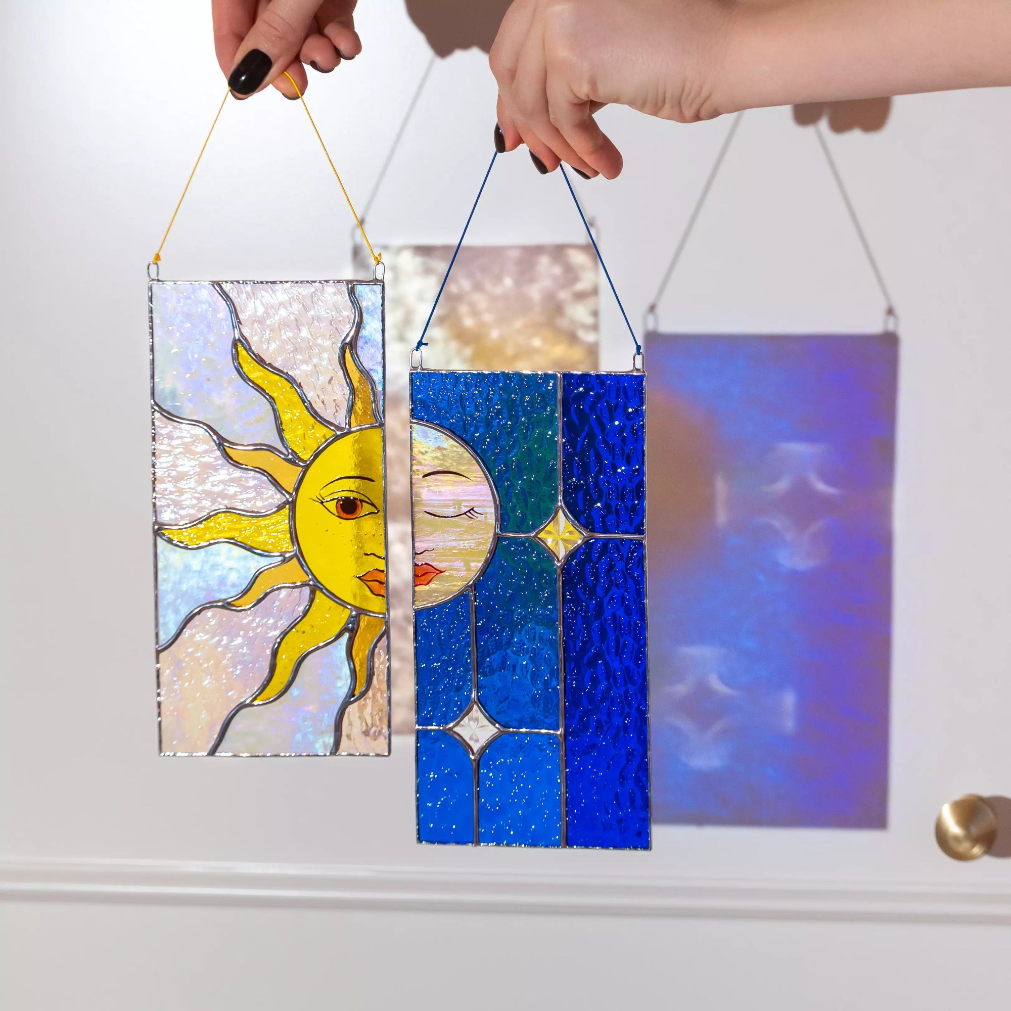 Hands holding a sun and moon stained glass suncatcher set with colorful shadows on the background.