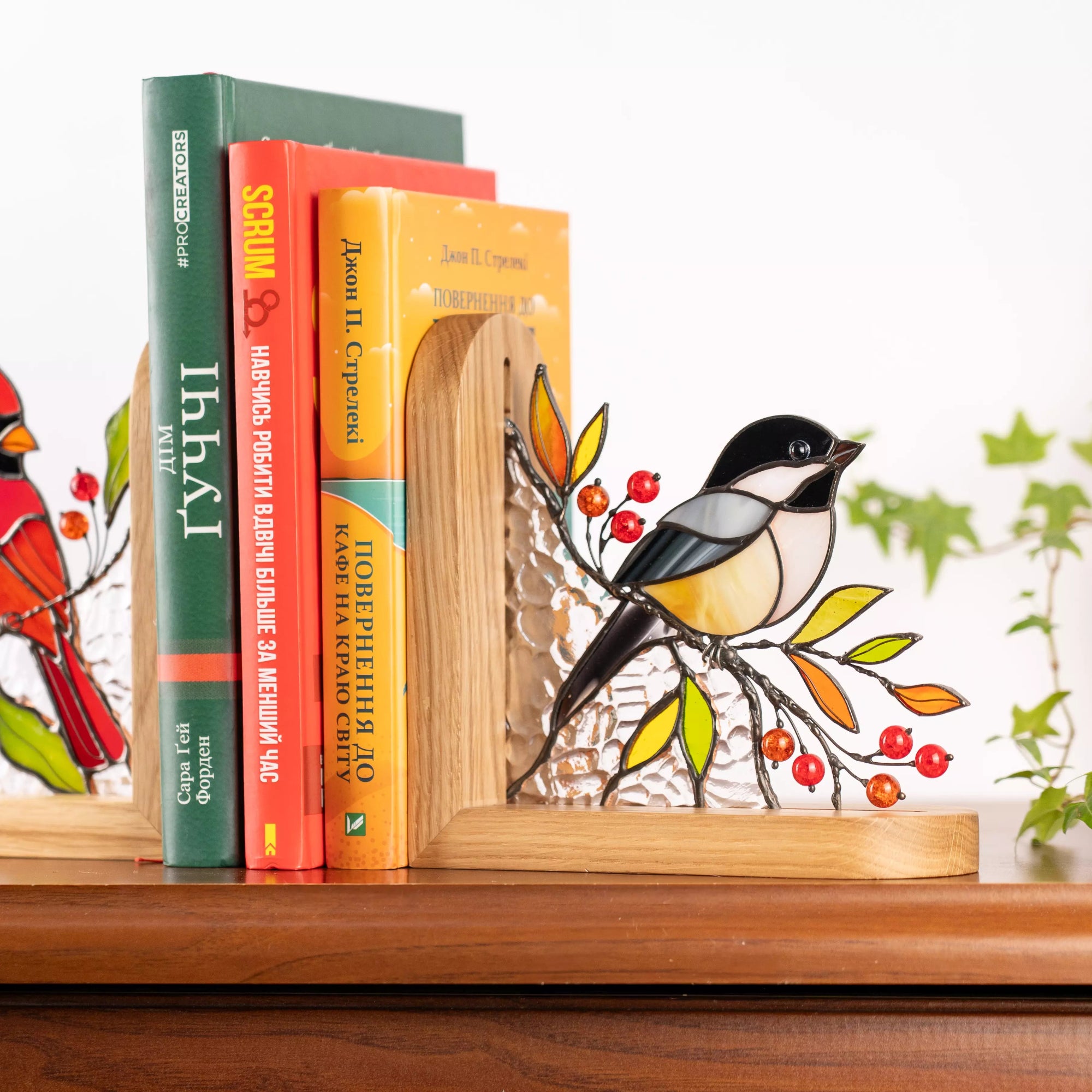 Stained glass chickadee bookend placed between books on a shelf, showing detailed bird design with red beads and wooden frame.