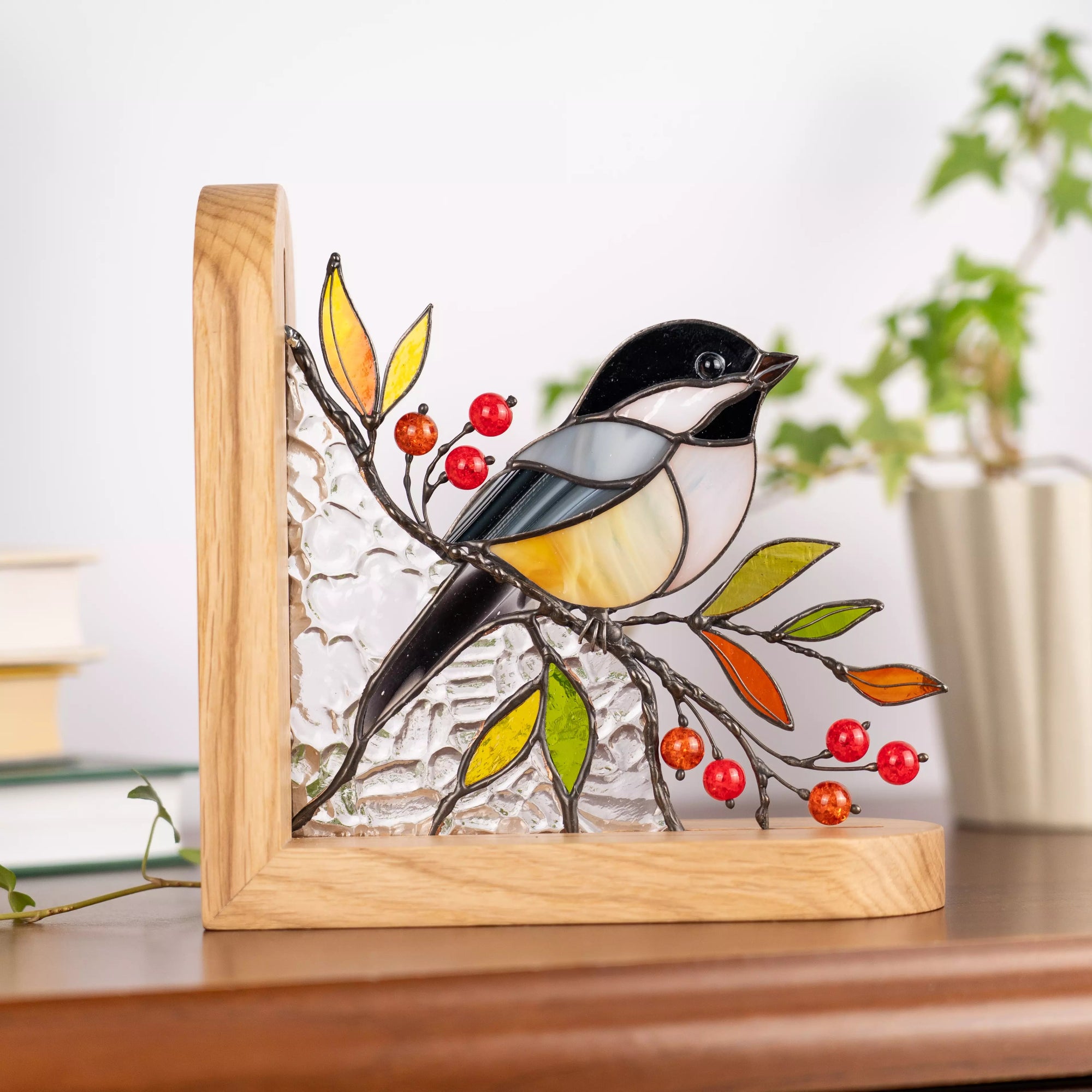 Stained glass chickadee bookend held in hands outdoors, highlighting bird details, colorful leaves, and red berries.