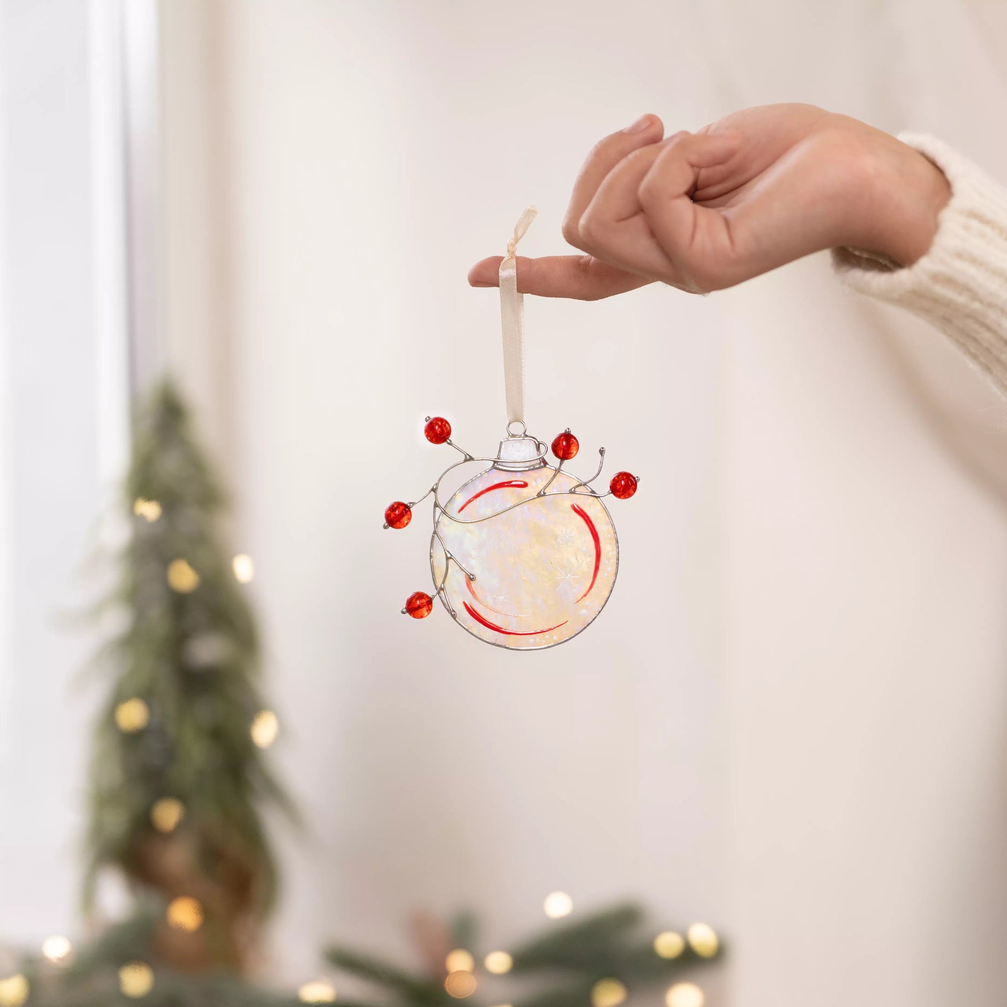 Stained glass Christmas ornament, with red berries and a sparkly finish hanging on a hand