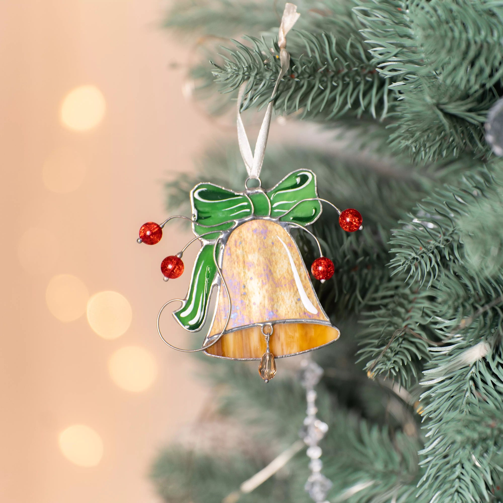 Christmas bell stained glass suncatcher with green bow and red berries hanging on a tree.