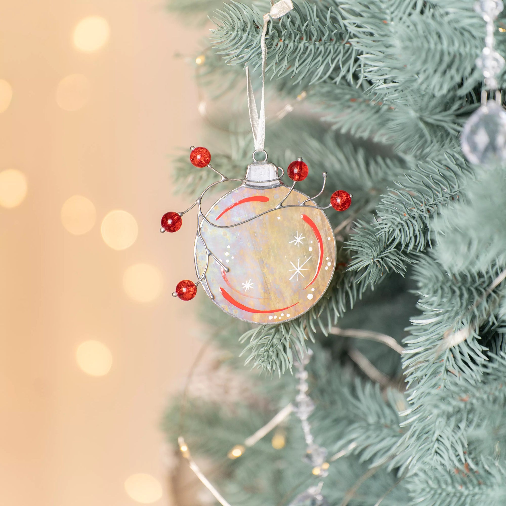 Stained glass Christmas ornament with red berries and glowing iridescent finish hanging by a ribbon