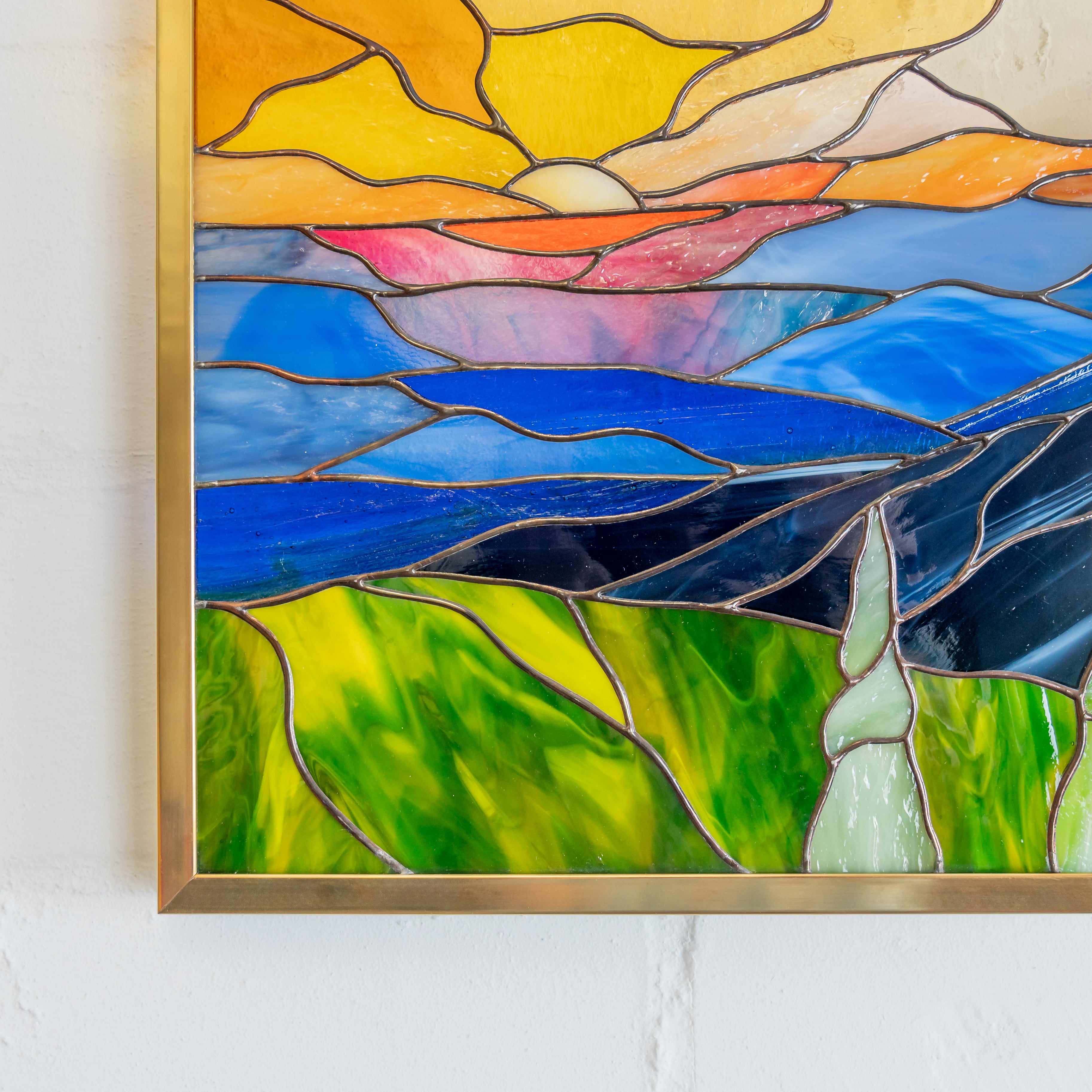 Colorful close-up of handmade stained glass panel showing yellow sun and layered mountain design