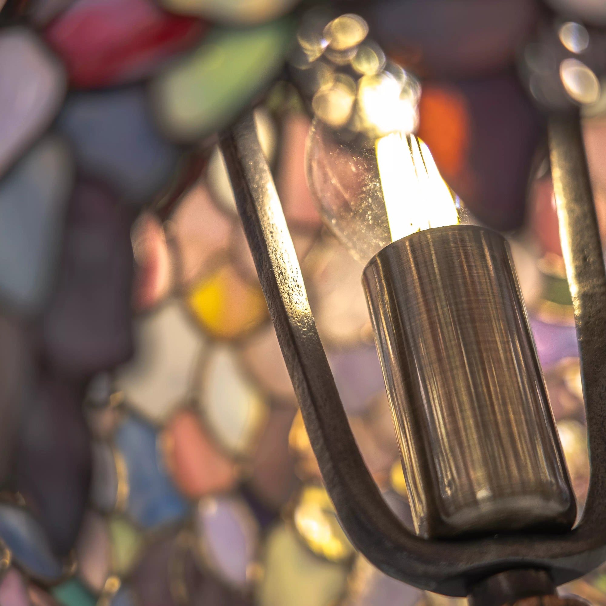 Close-up of a light bulb with a pastel colorful stained glass lamp details in the background