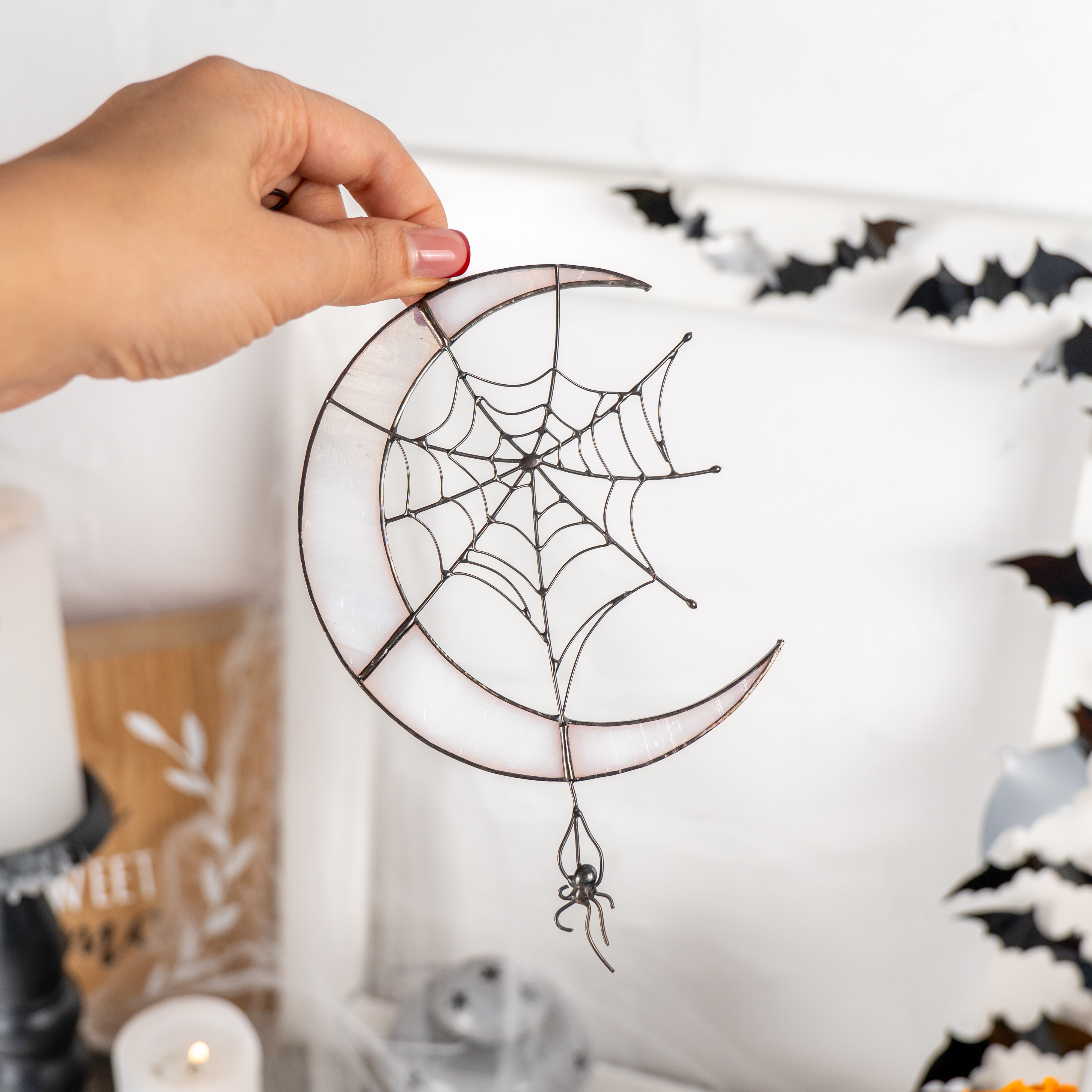 Hand holding the stained glass crescent  moon and web suncatcher among black bat decorations 
