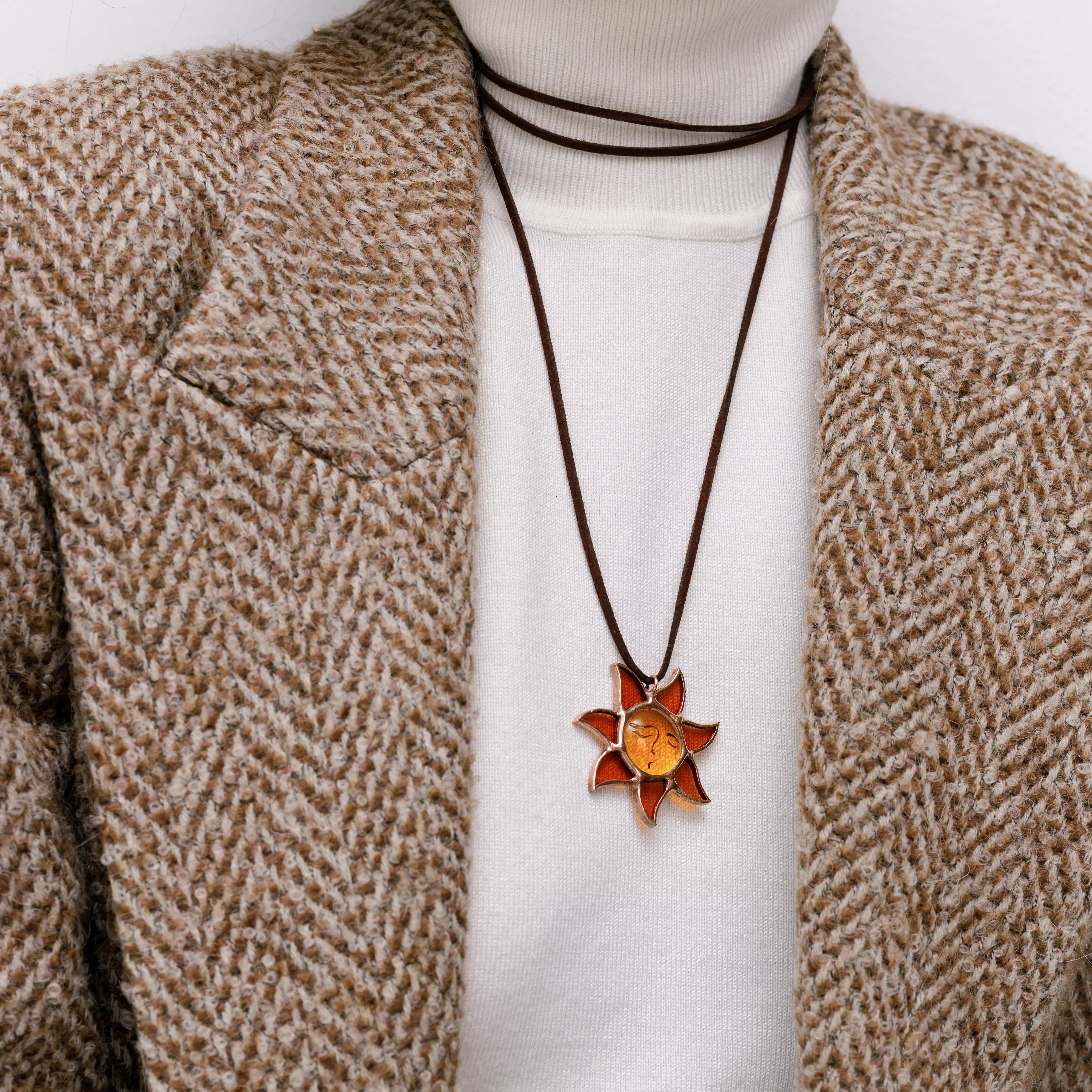 Stained glass sun pendant with amber glass and suede cord, styled with a beige wool coat