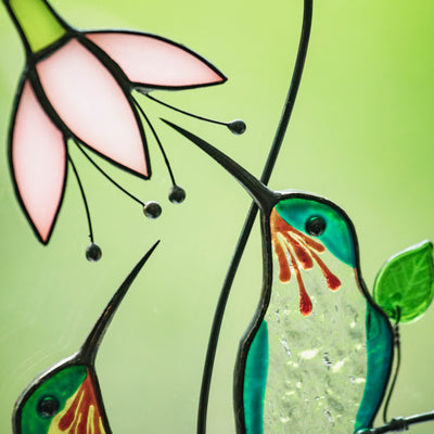 Close-up of a stained glass green hummingbird with a pink flower.