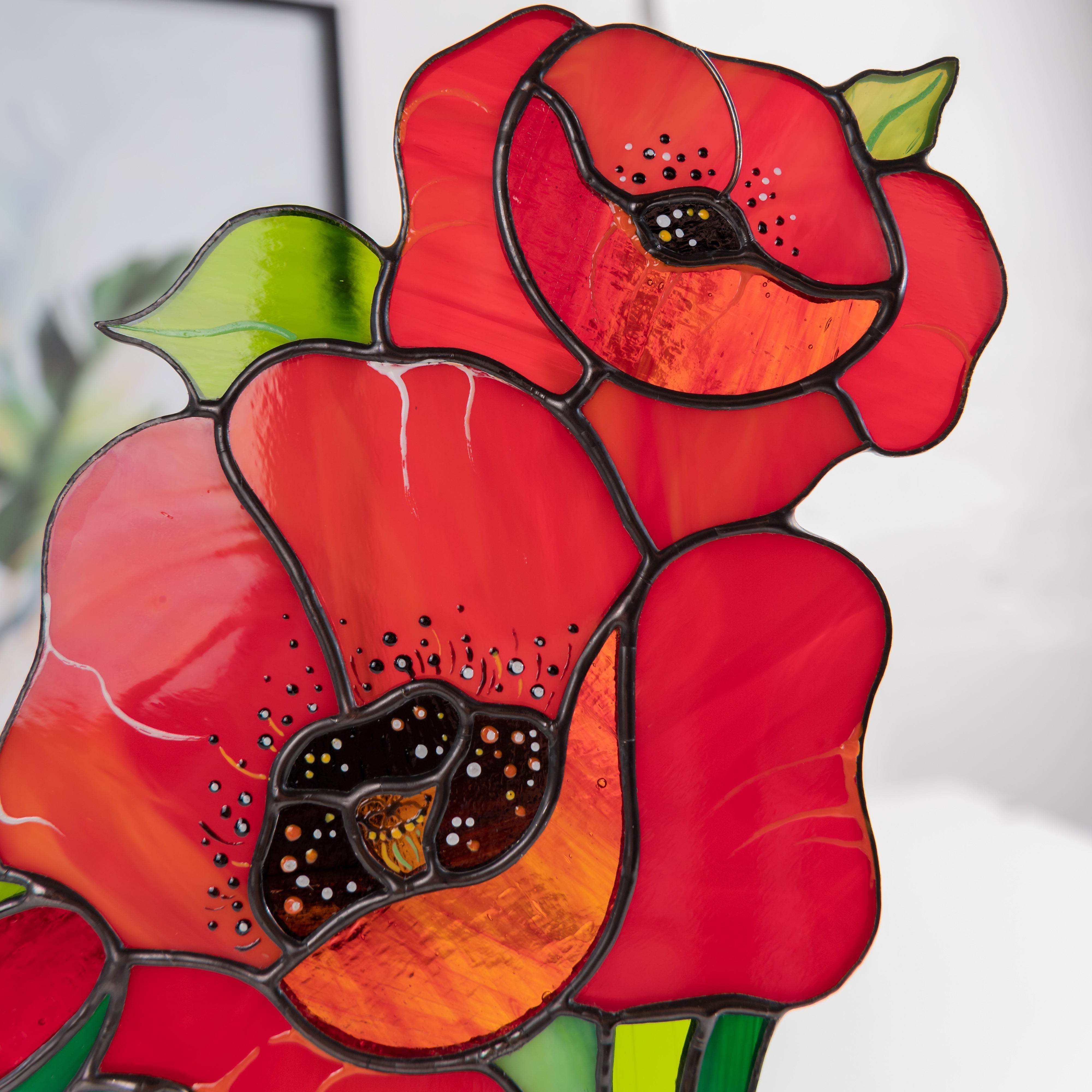 Detailed view of two red stained glass poppy flowers with black centers and orange accents.