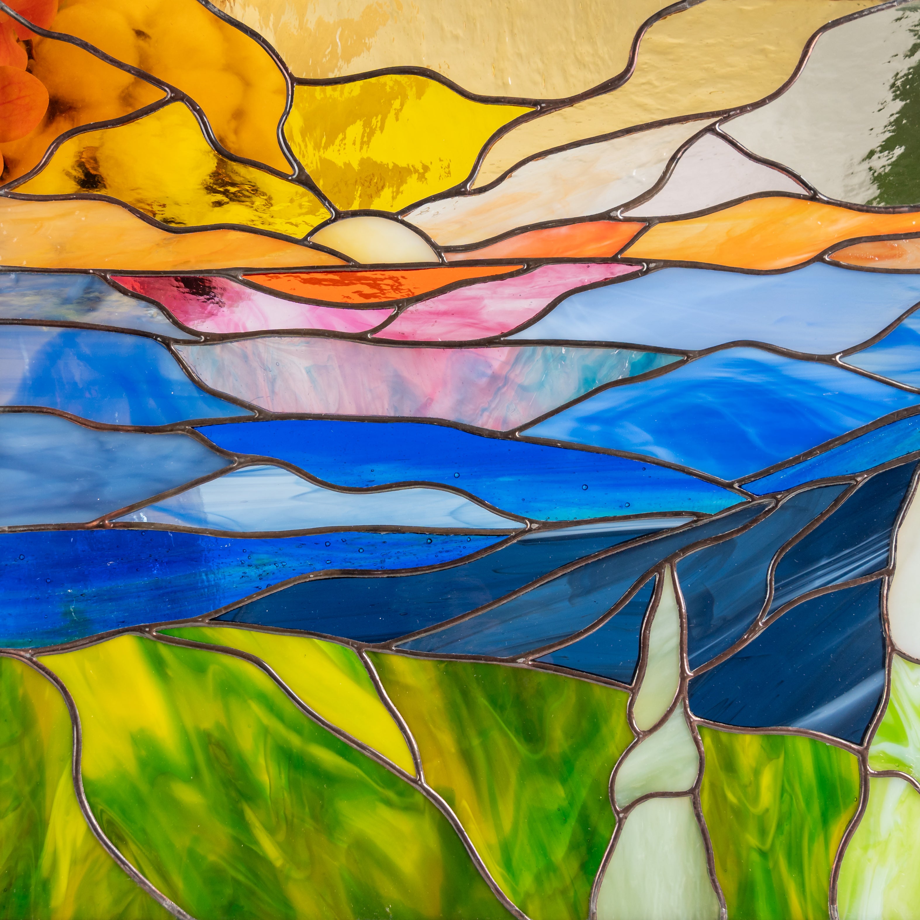 Detailed view of handmade stained glass panel with green, blue, and amber mountain layers