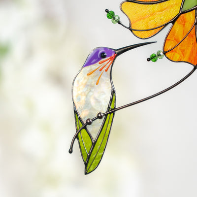 Detailed view of stained glass hummingbird with shimmering body and orange flower in soft light