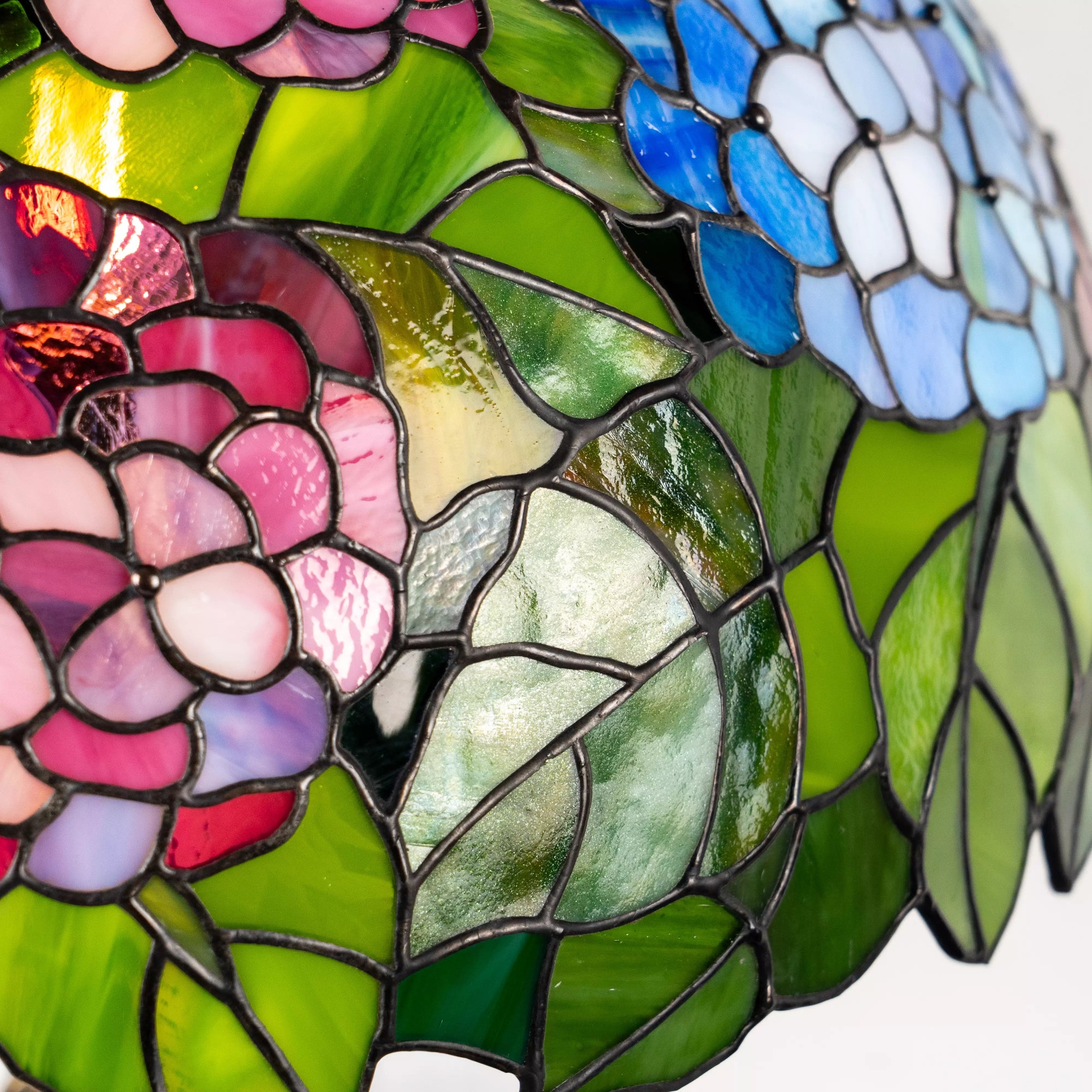 Detailed view of stained glass hydrangea flowers and green leaves, showing texture and color variations