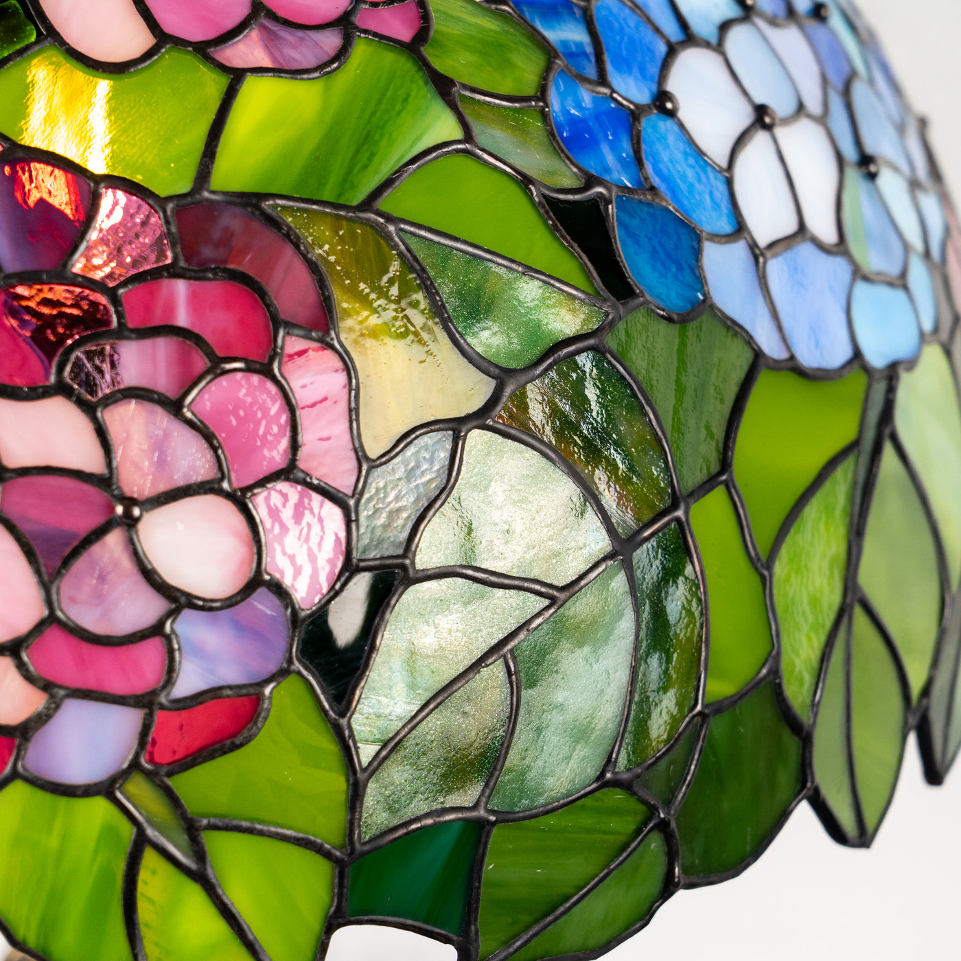 Detailed view of stained glass hydrangea flowers and green leaves, showing texture and color variations