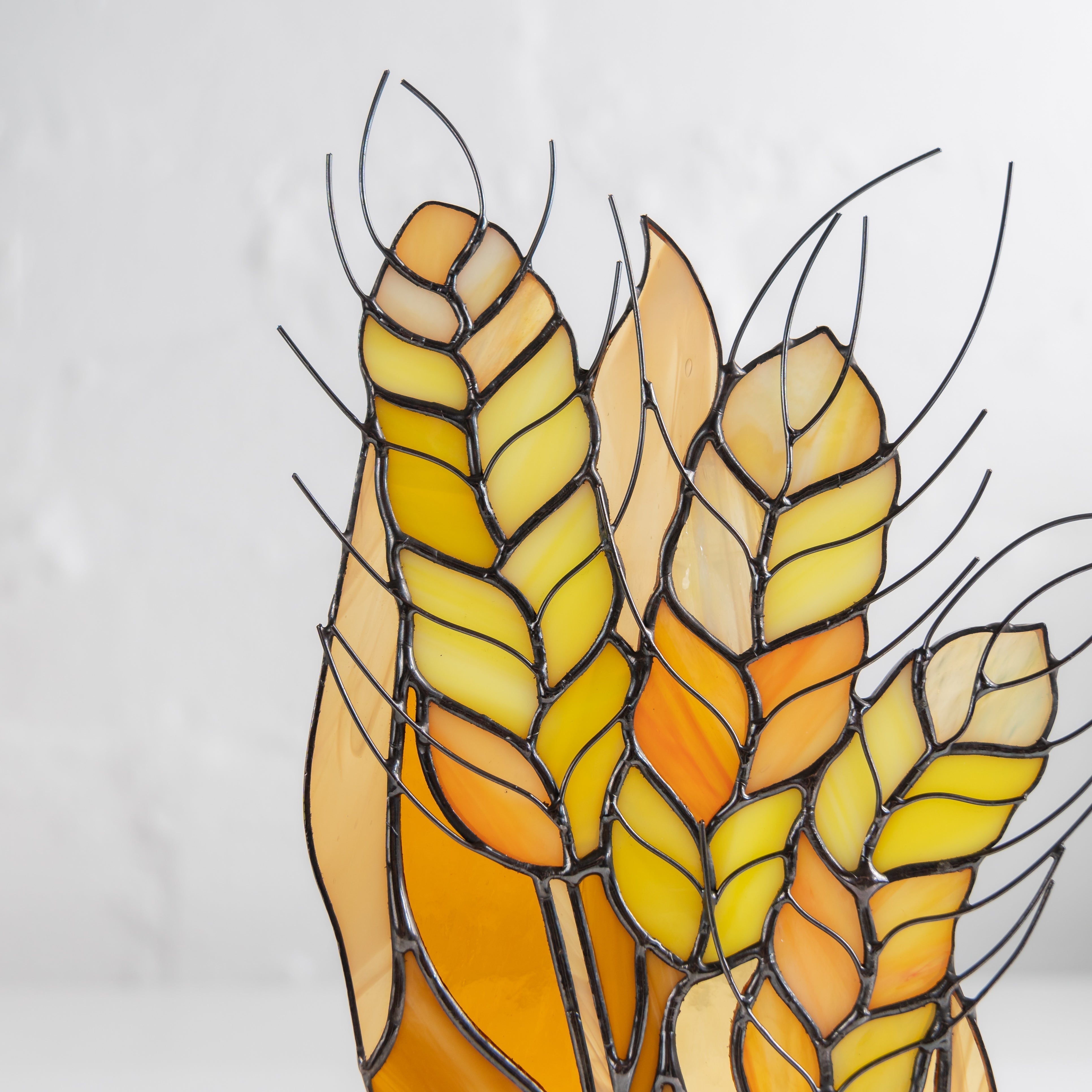 Detail view of stained glass wheat showing individual yellow and orange grain segments in metal outlines.