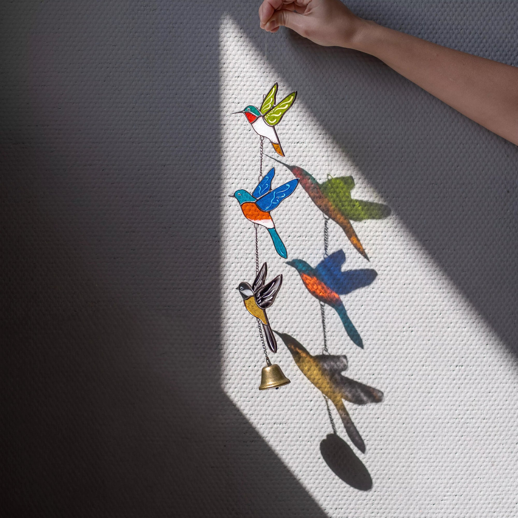 Stained glass bird-shaped wind chime with a bell on a gray background
