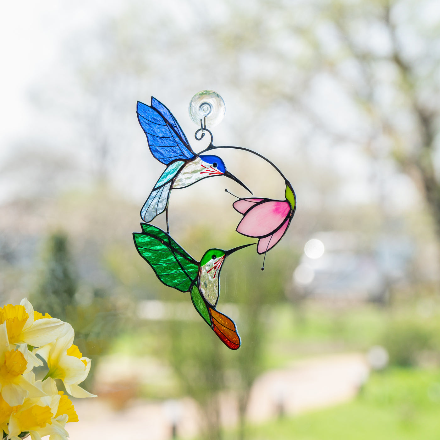 Suncatcher with green and blue hummingbirds on window.
