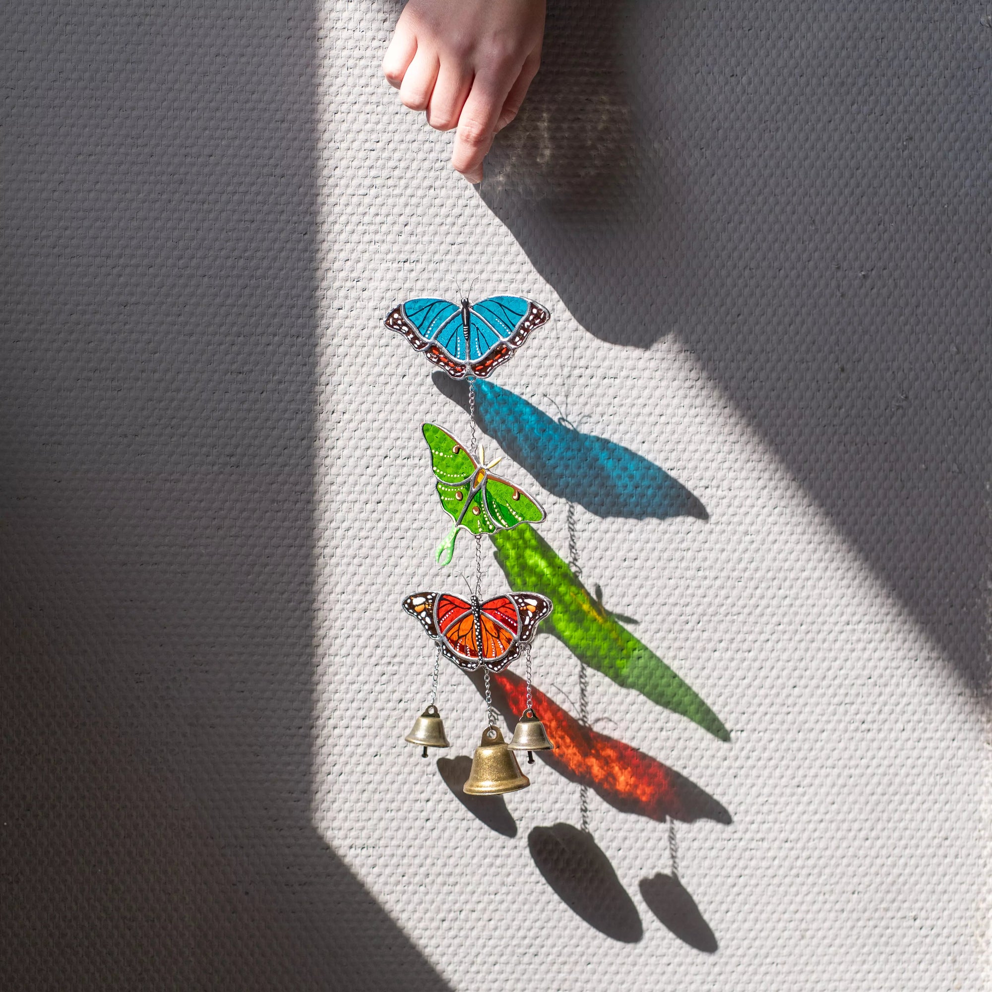 Colorful butterfly stained glass wind chime with bells on a textured surface