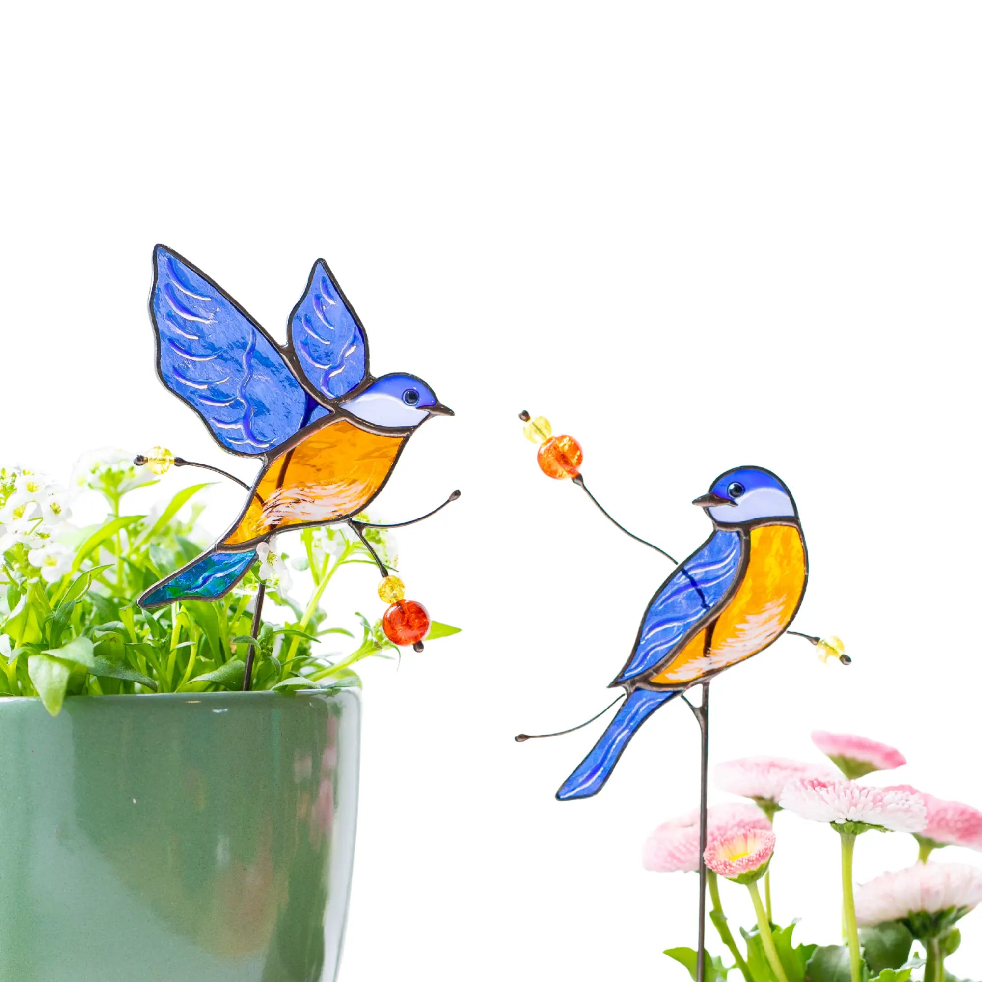 Stained glass bird plant stakes with flowers and a pot in the background.