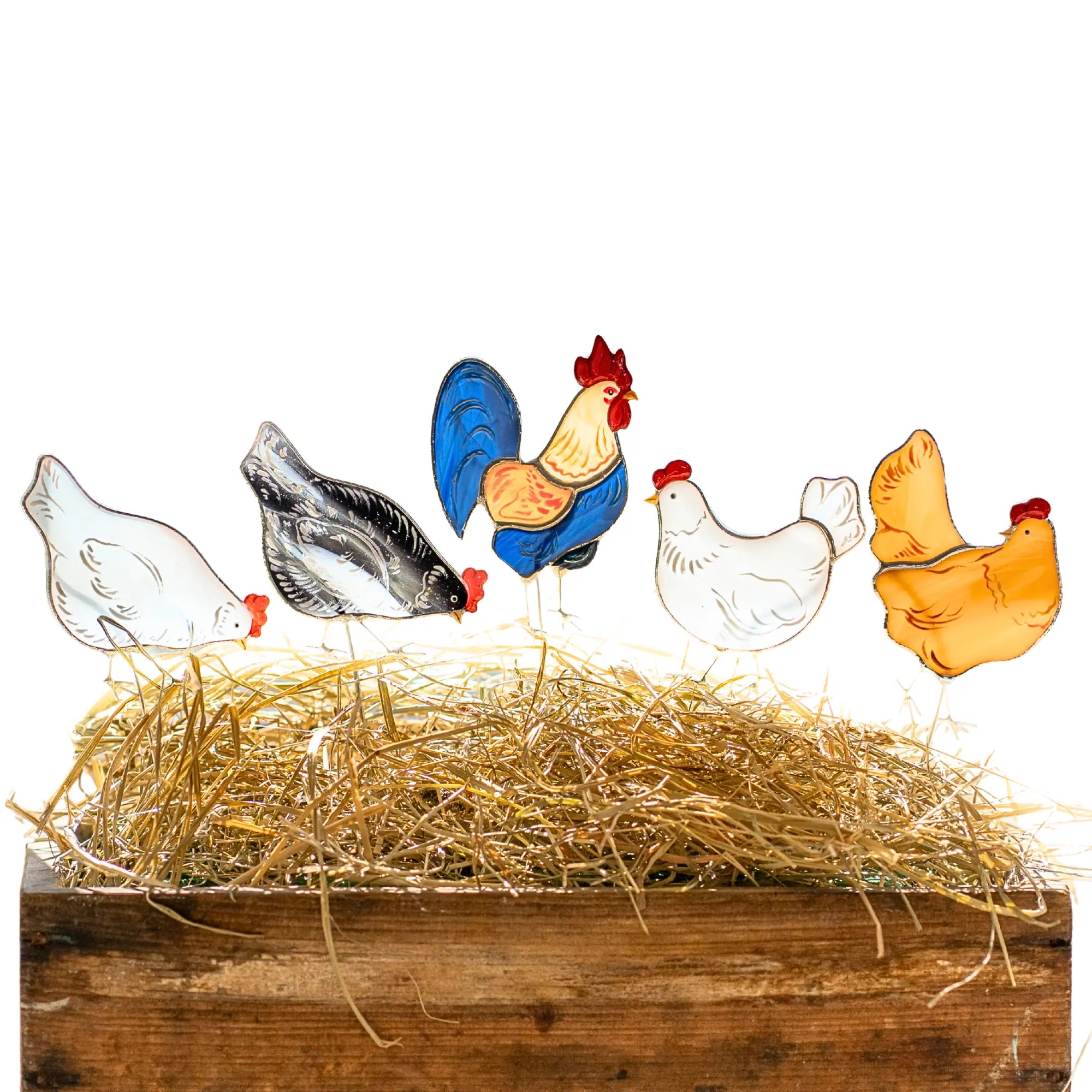 Colorful stained glass chicken plant stakes on a bed of straw with a wooden base.