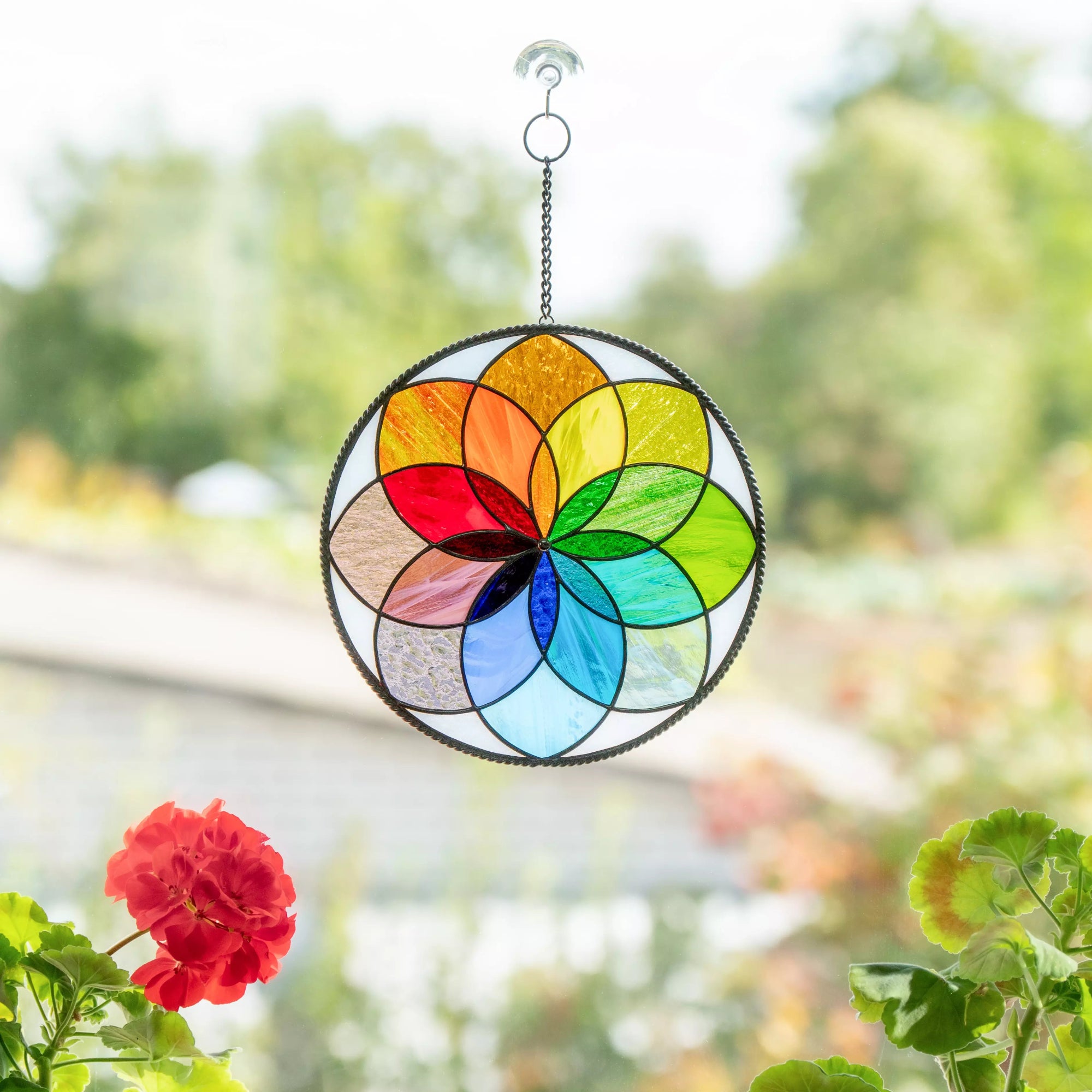 Rainbow stained glass mandala hanging on window with flowers in background
