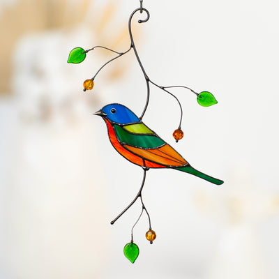 Bright stained glass bunting bird hanging with green glass leaves and amber beads on metal branches.