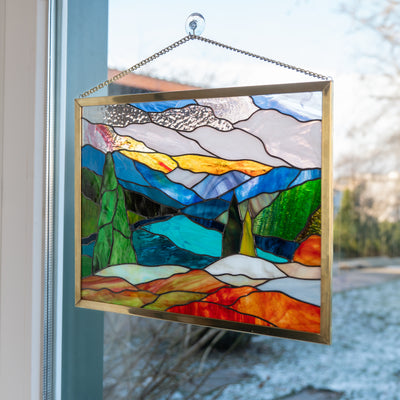handmade stained glass Mt. Rainier panel is hanging on a window 