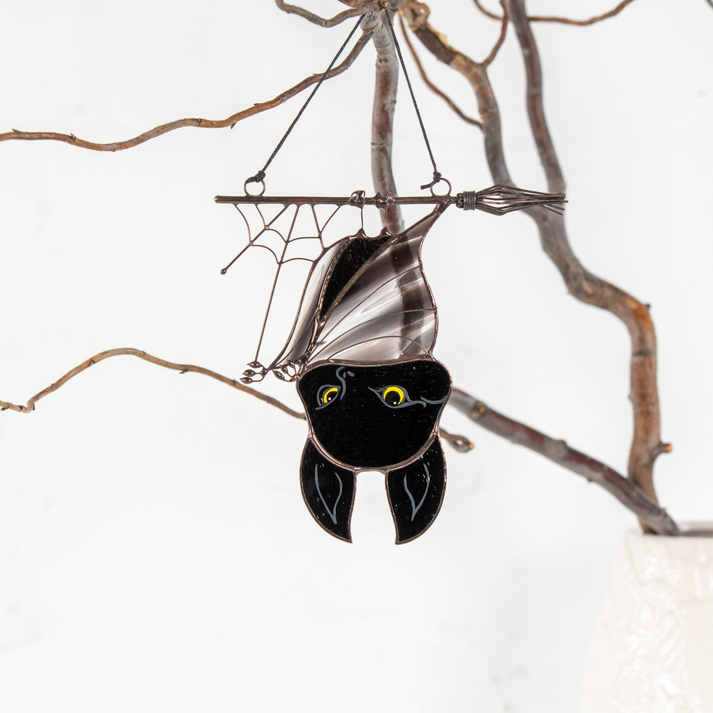 cute black bat made of stained glass is hanging on the witch broom