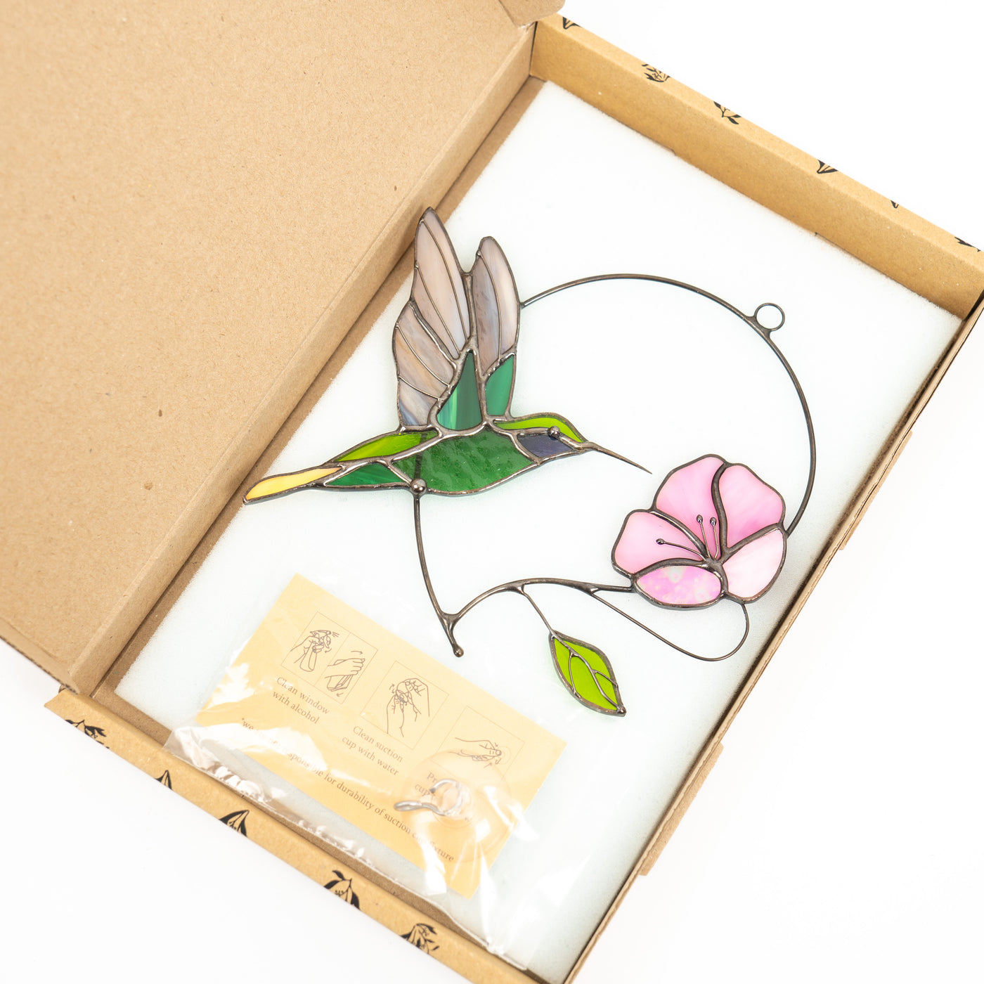 hummingbird with the pink flower stained glass window hanging in the brand box of Glass Art Stories 