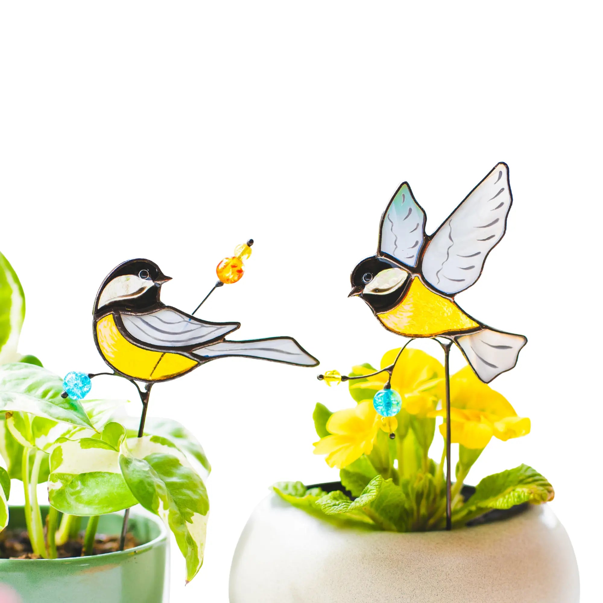 Stained glass chickadee plant stakes on plants with a white background