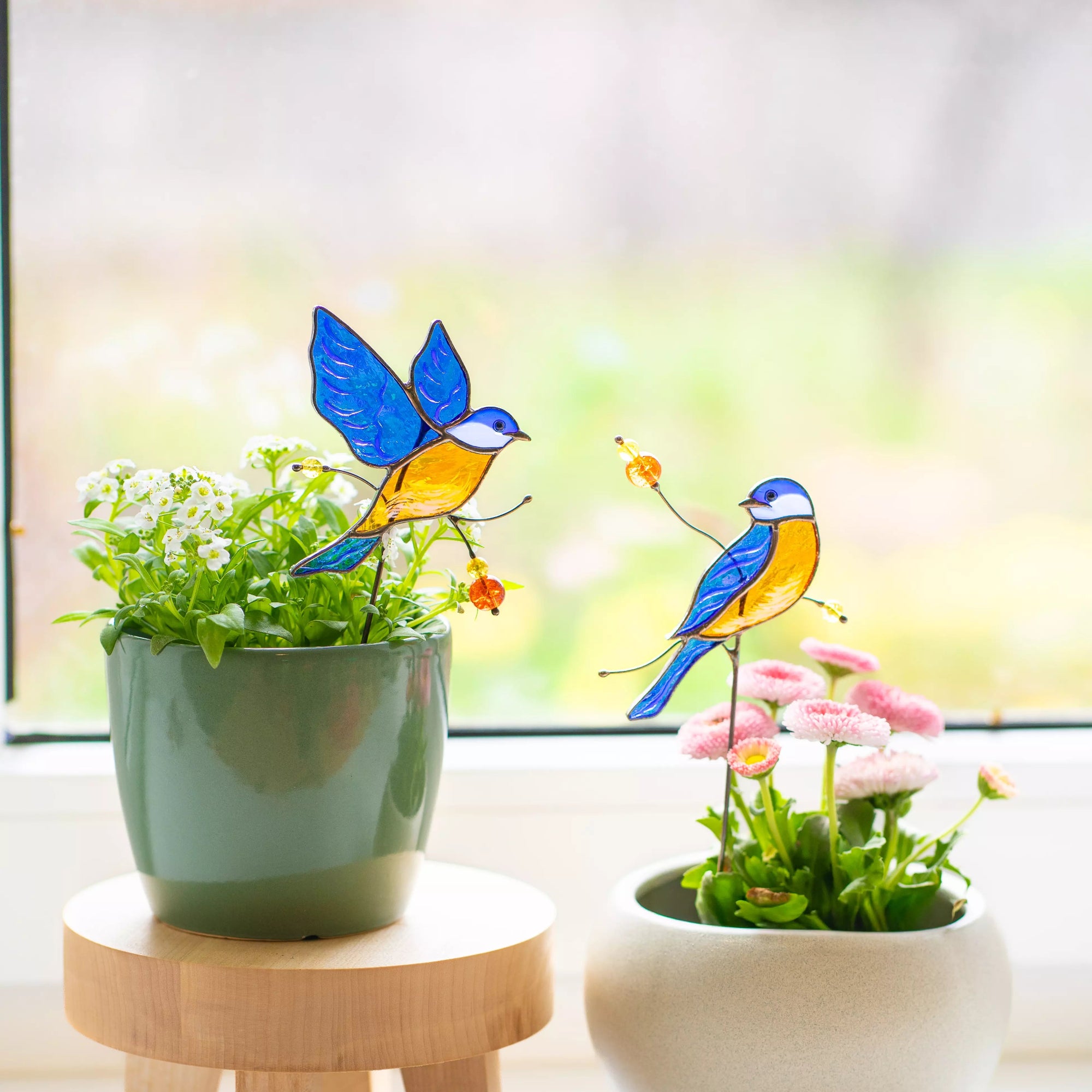 Stained glass bluebirds on stands with plants in the background