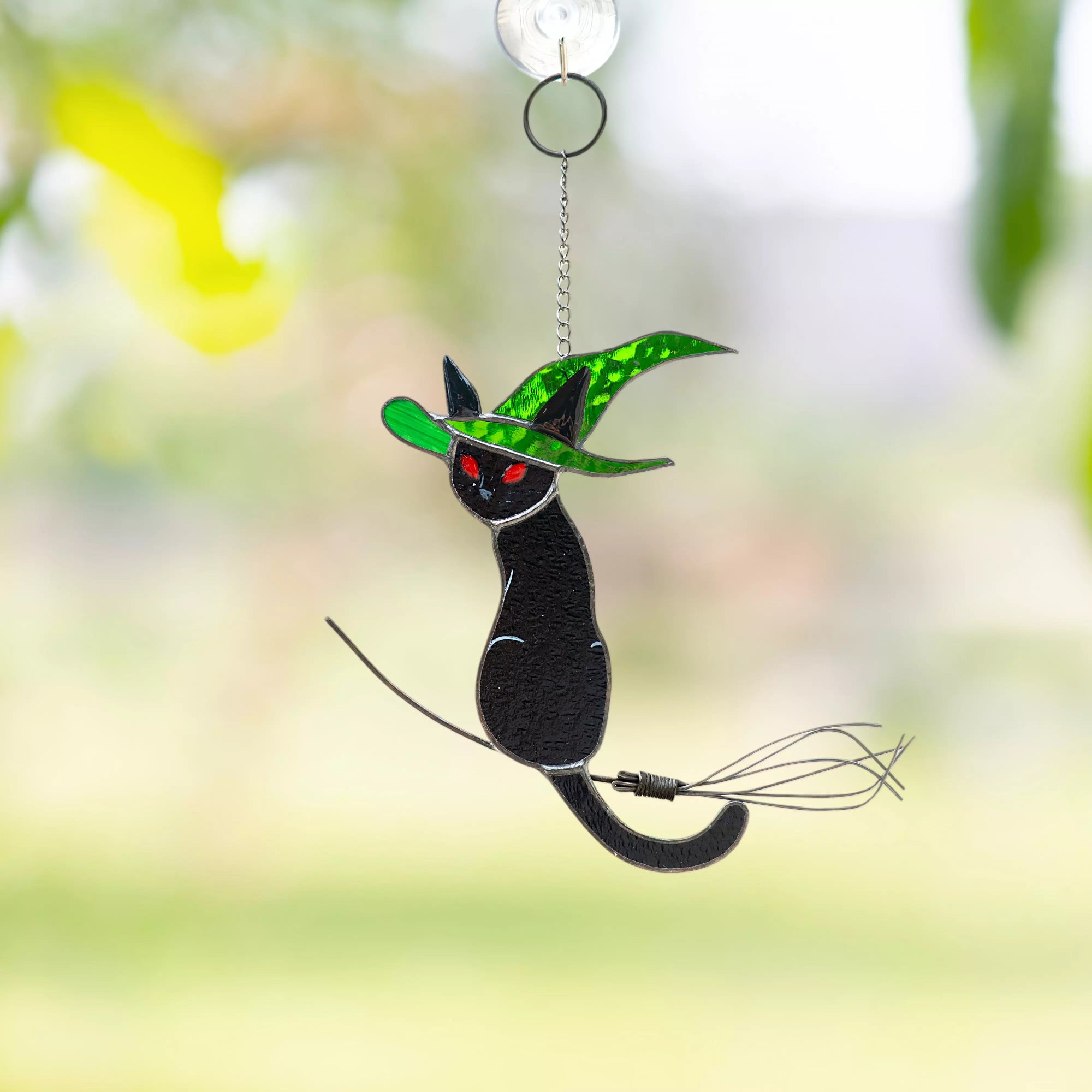 Decorative stained glass black cat with green hat suncatcher hanging on a window against a blurred natural background
