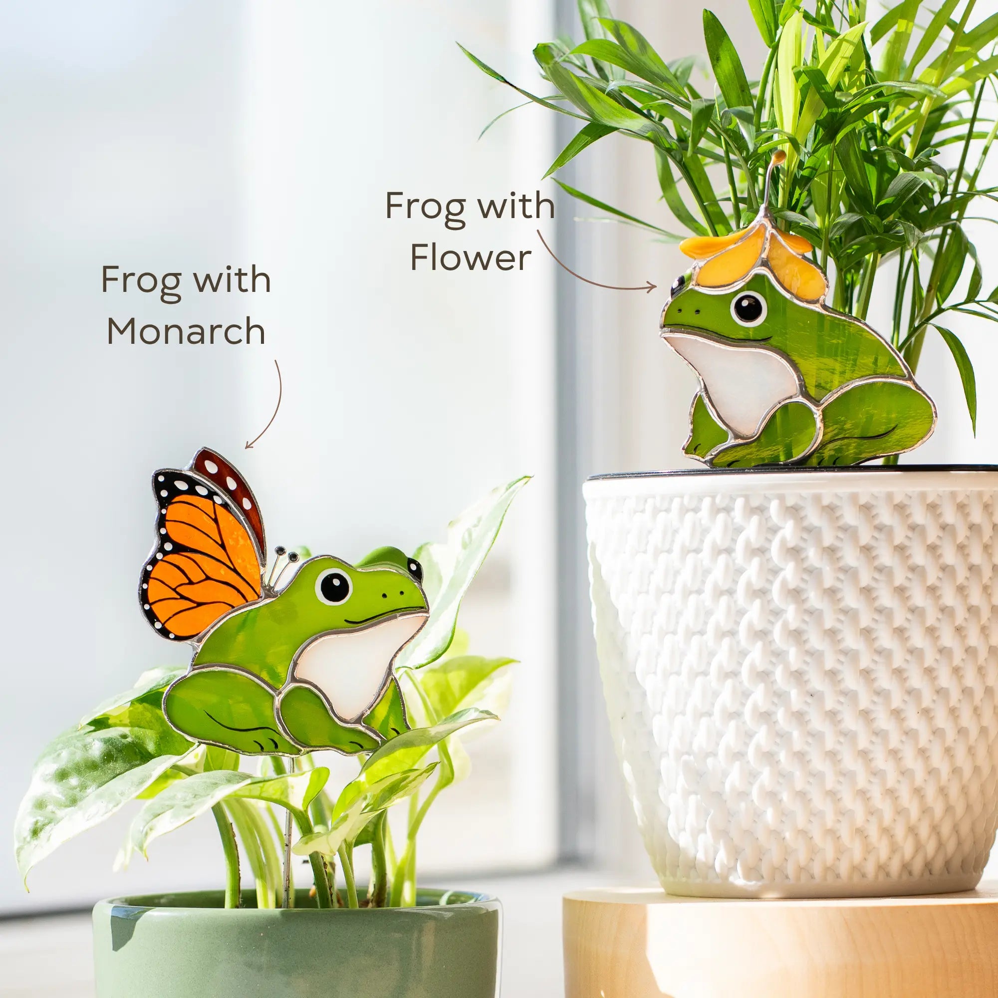 Stained glass frog plant stakes with a butterfly and flower on top of a plant in a pot.