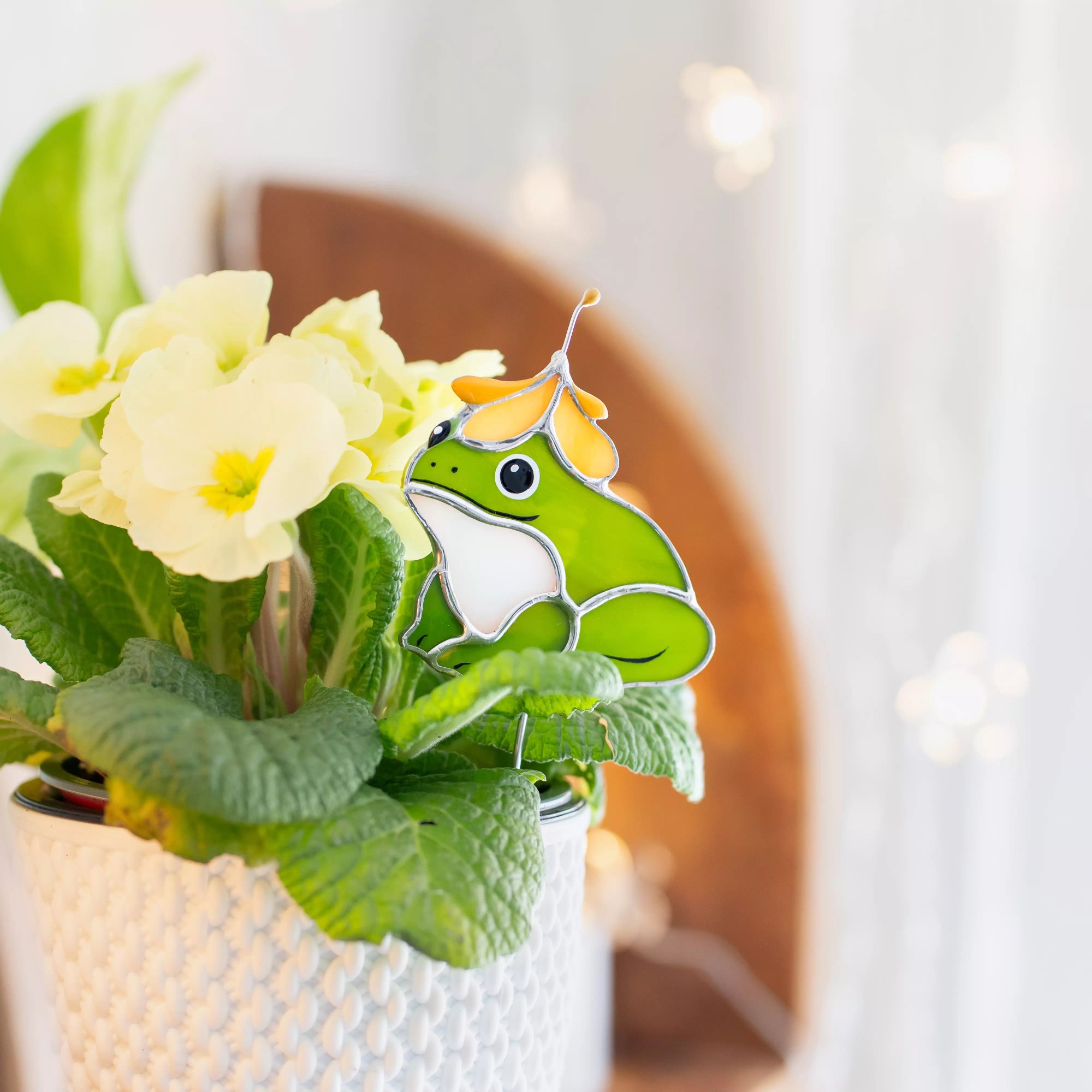Stained glass frog plant stake on a potted plant with a blurred background