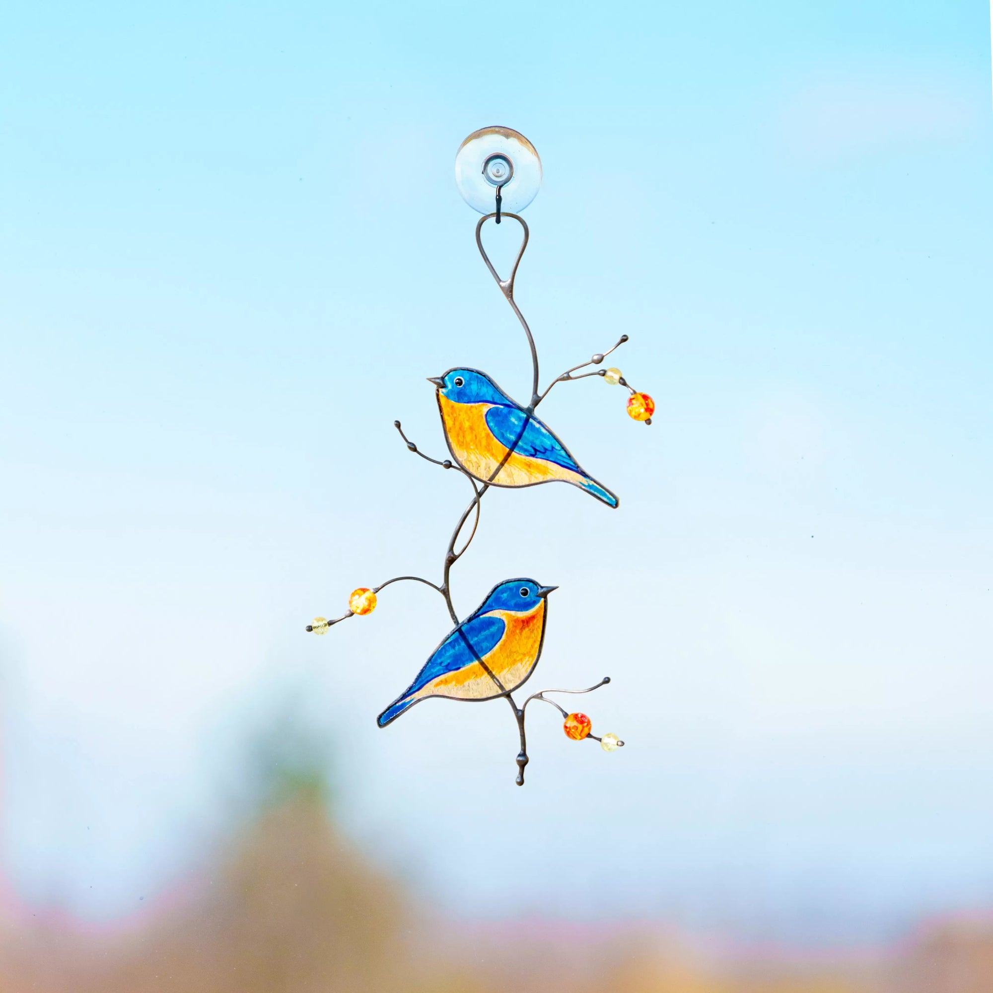 Stained glass bird ornament on a branch against a blue sky background