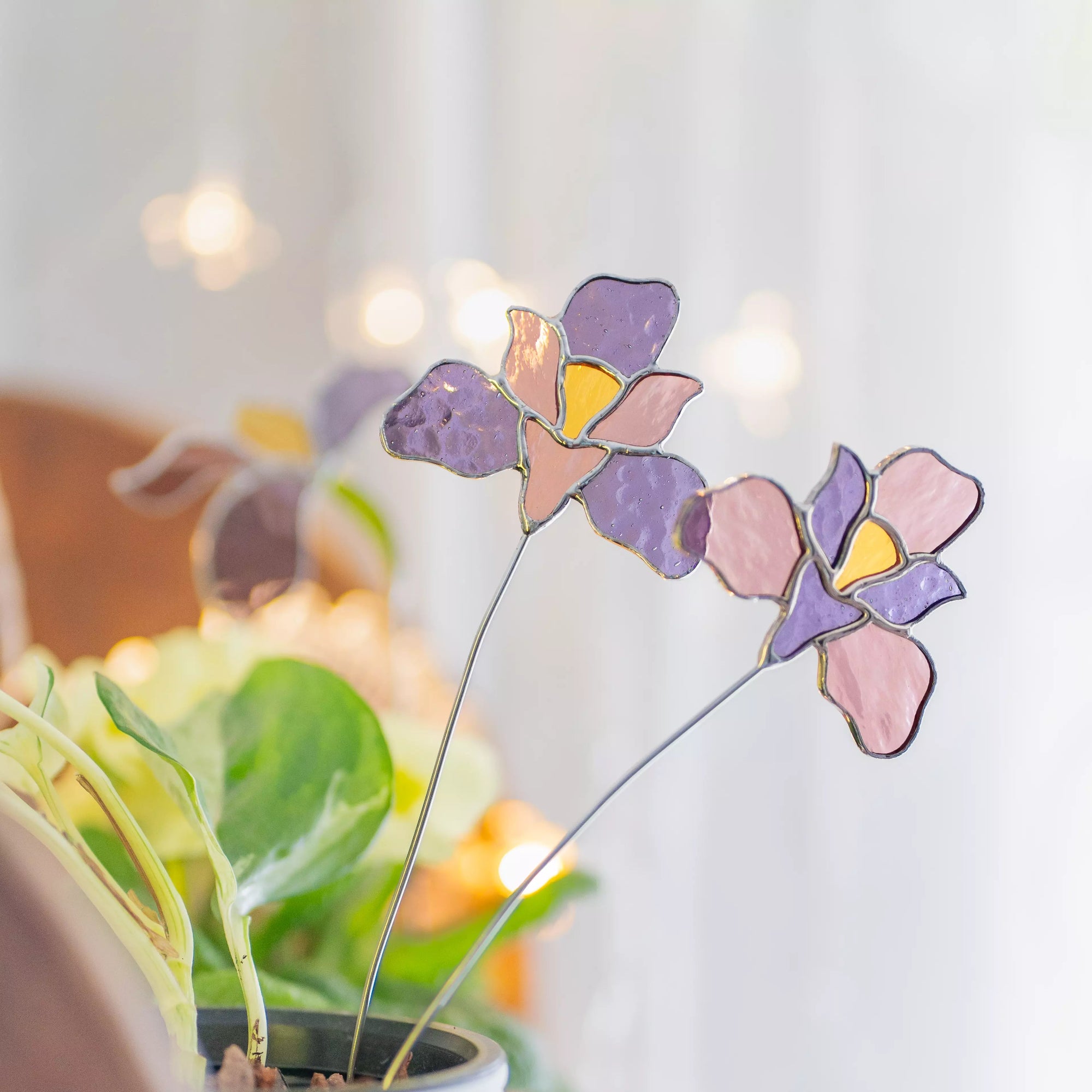 Stained glass iris flower plant stakes with purple and pink colors in a blurred indoor setting