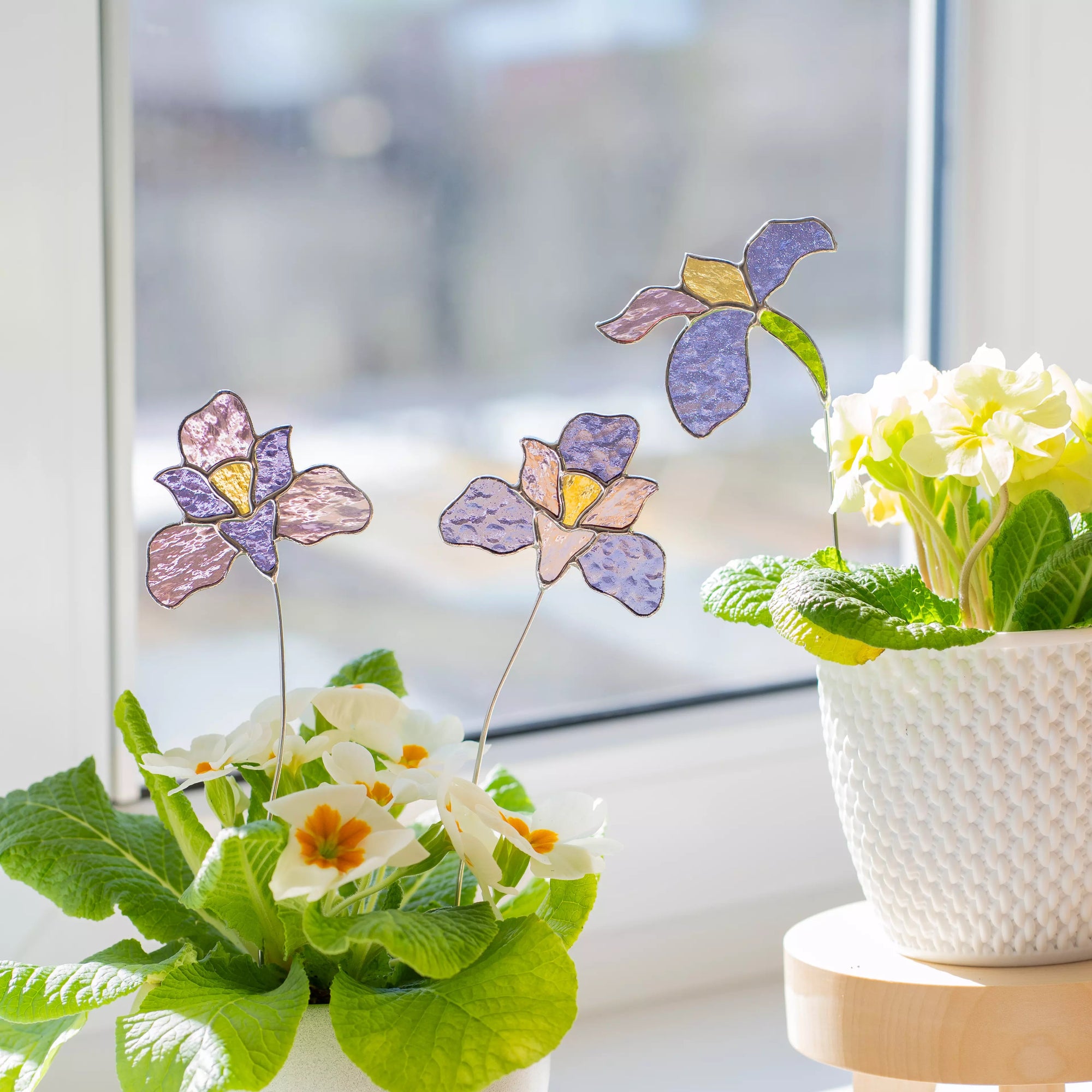 Stained glass plant stakes featuring iris flowers in front of a potted plant with a blurred window background