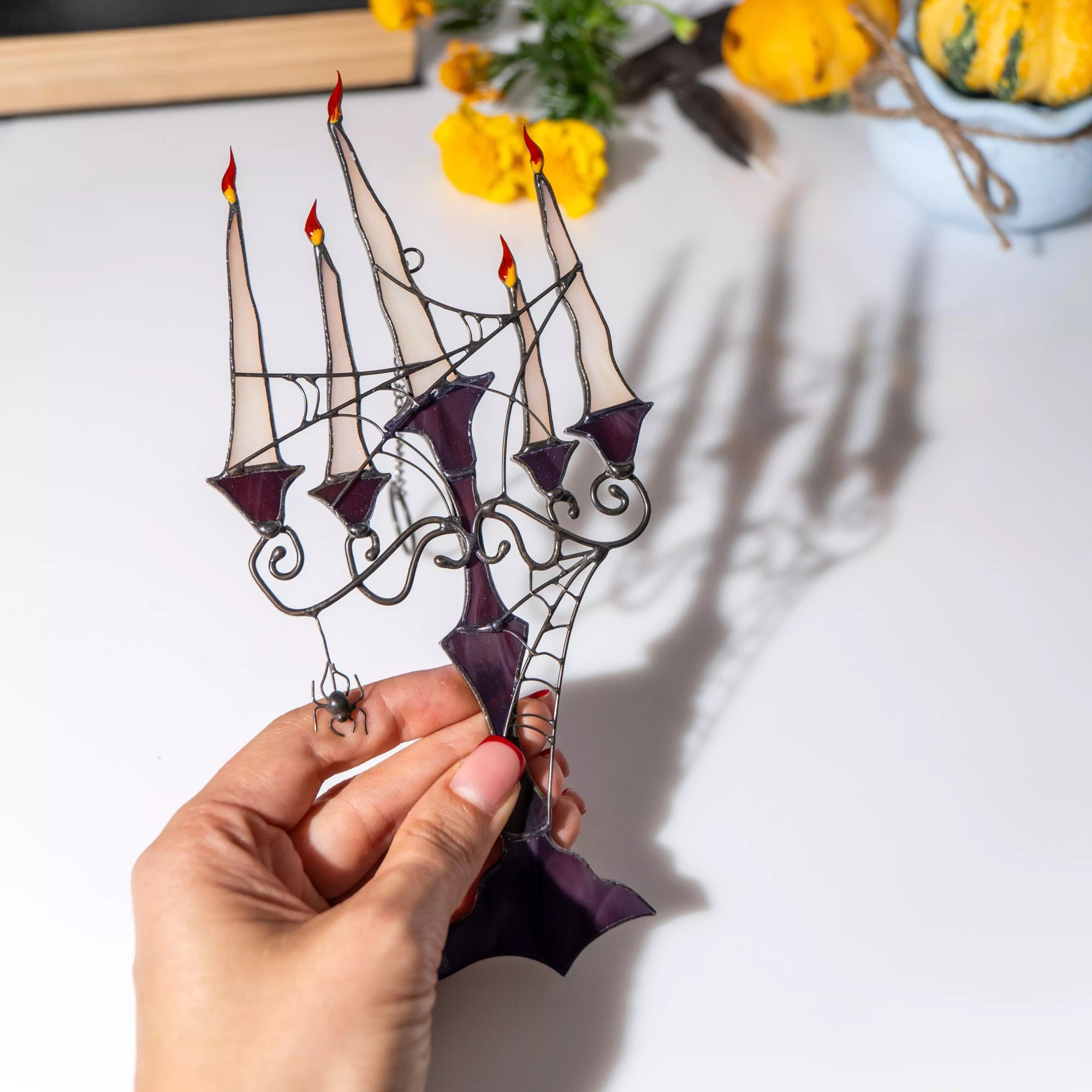 Stained glass panel with candles held by a hand, casting soft shadow on a white background