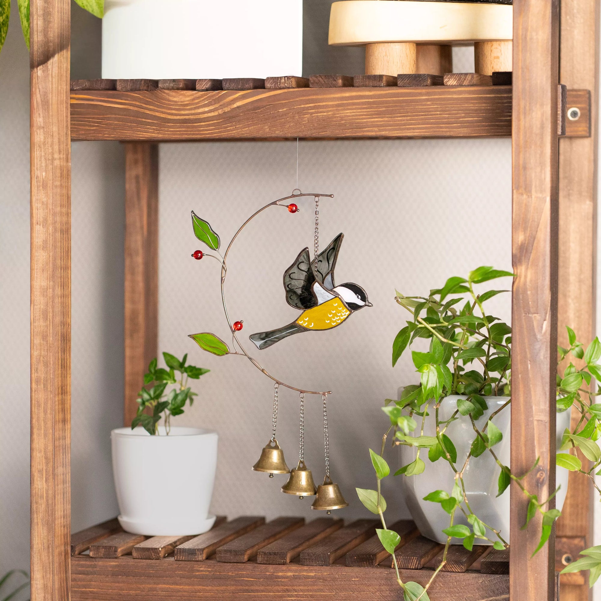 Stained glass wind chime hanging bird ornament on a wooden shelf with plants