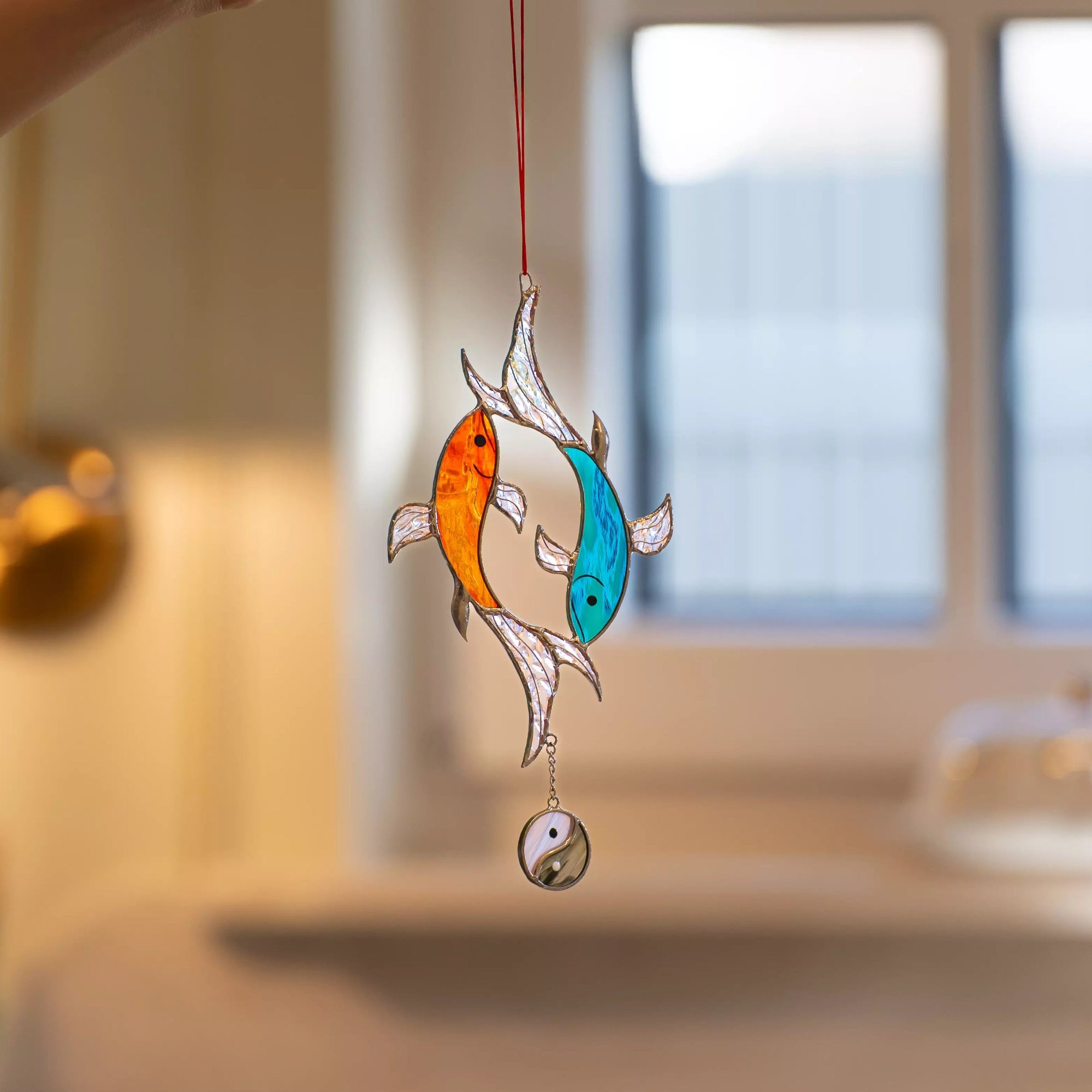 Decorative stained glass ornament with two colorful fish and a yin yang symbol, held by a hand.