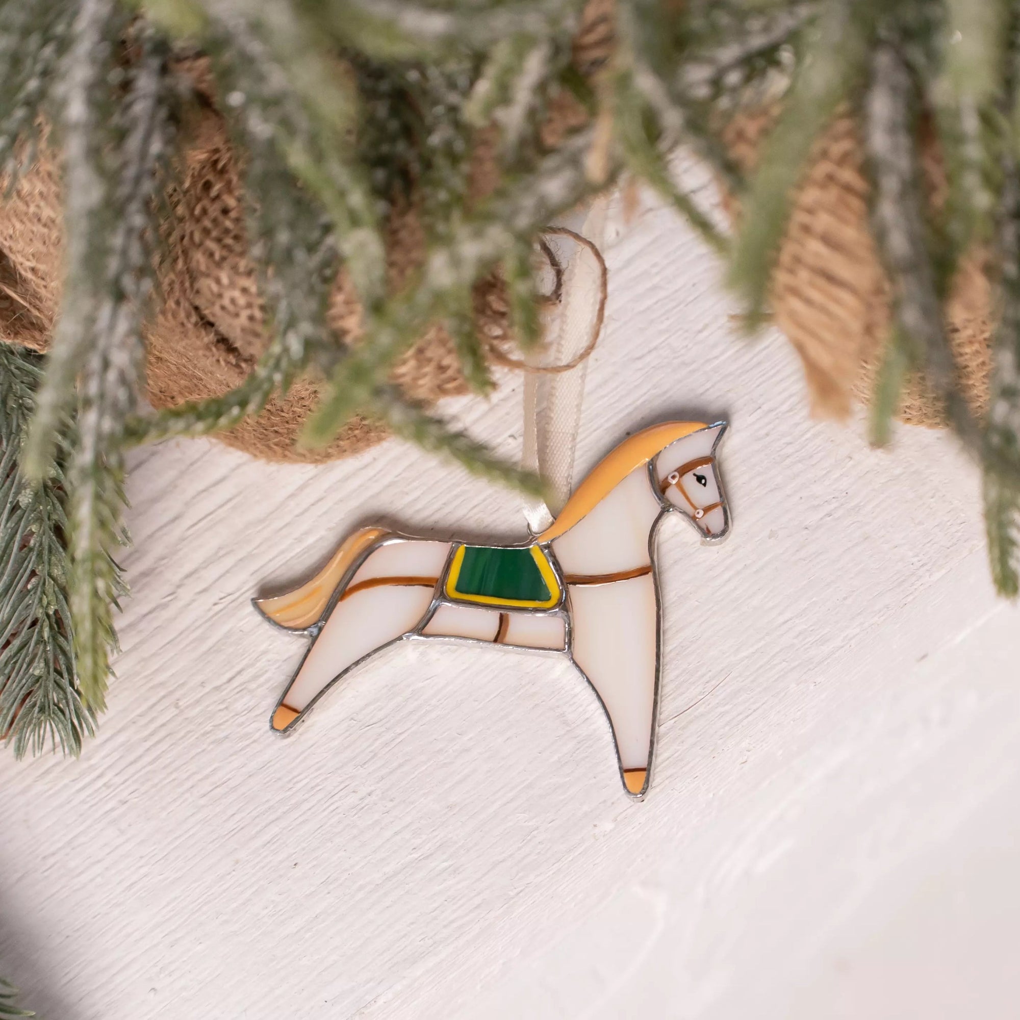 Beige horse stained glass ornament lies near a Christmas tree