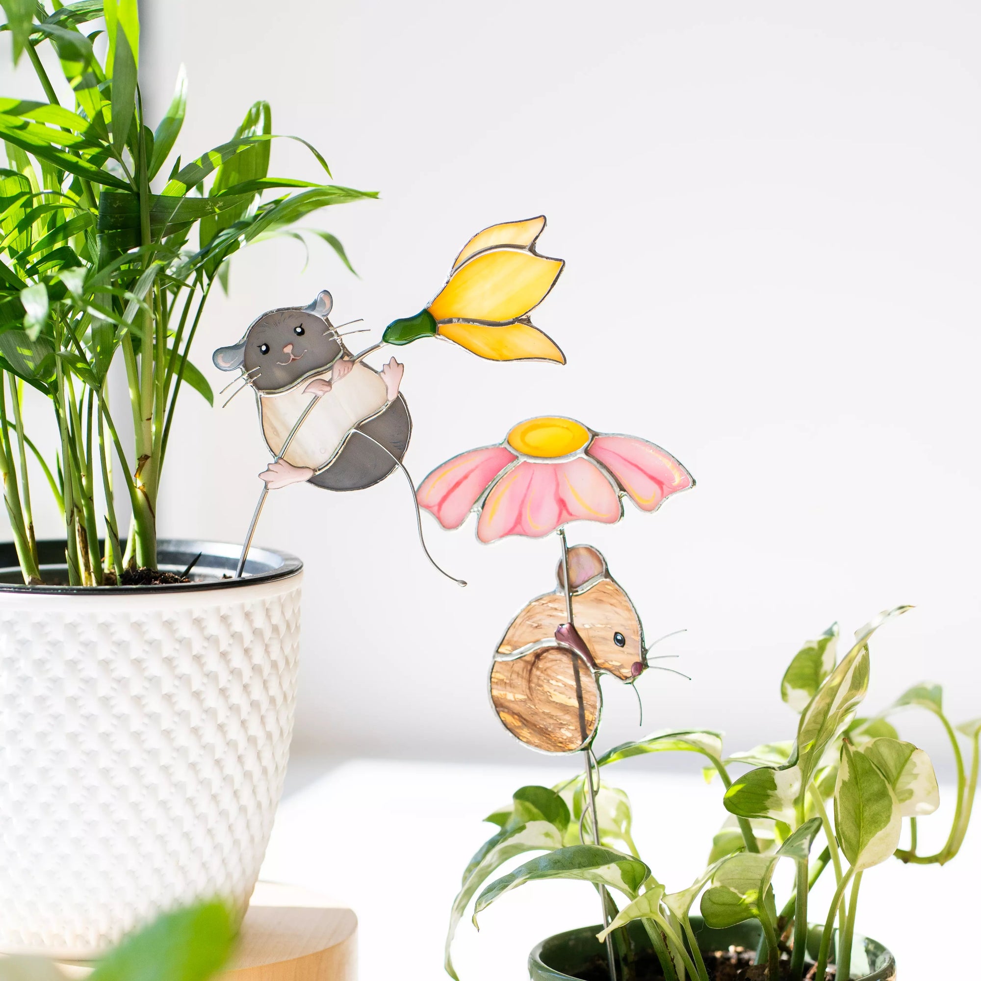 Stained glass mice and flower plant stakes with a potted plant in the background