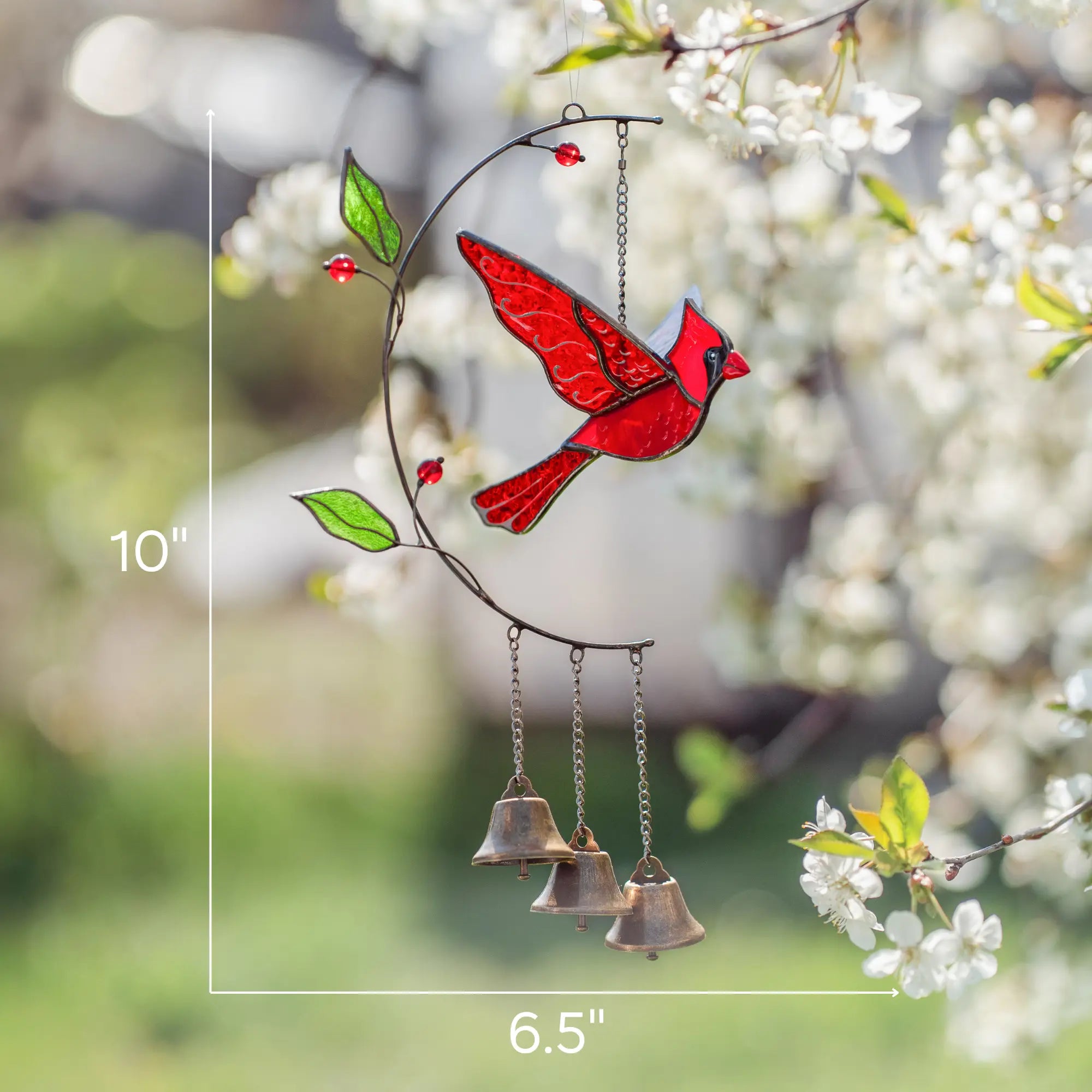Stained glass red cardinal bird ornament with bells on a branch against a blurred natural background