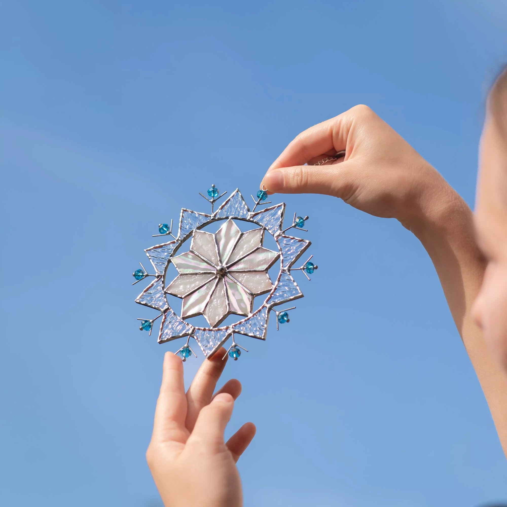 Decorative stained glass snowflake ornament held by hands against a clear blue sky